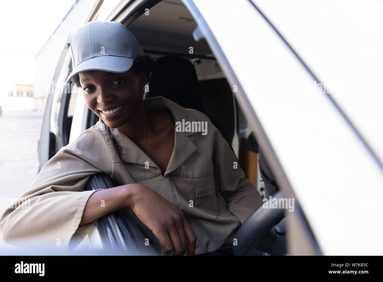 Delivery woman looking at camera while sitting in front seat of van outside the warehouse Stock Photo