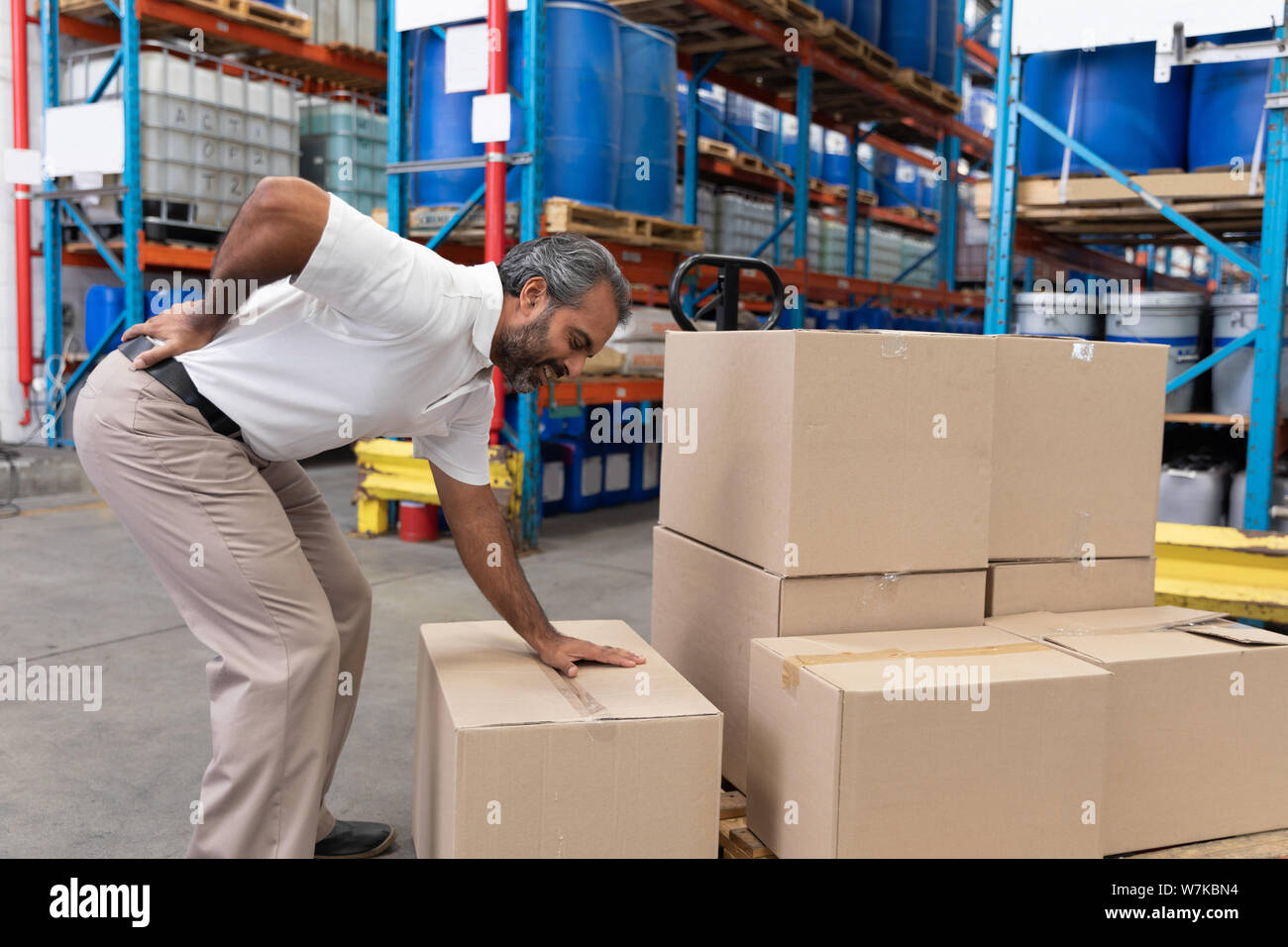 Male staff suffering from back pain while holding heavy cardboard box Stock Photo