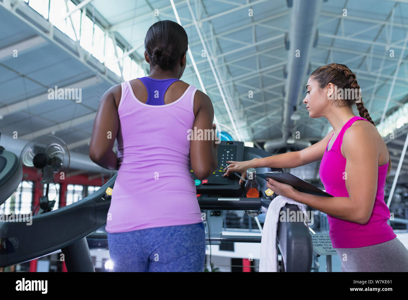 Female trainer assisting woman to work out on treadmill Stock Photo