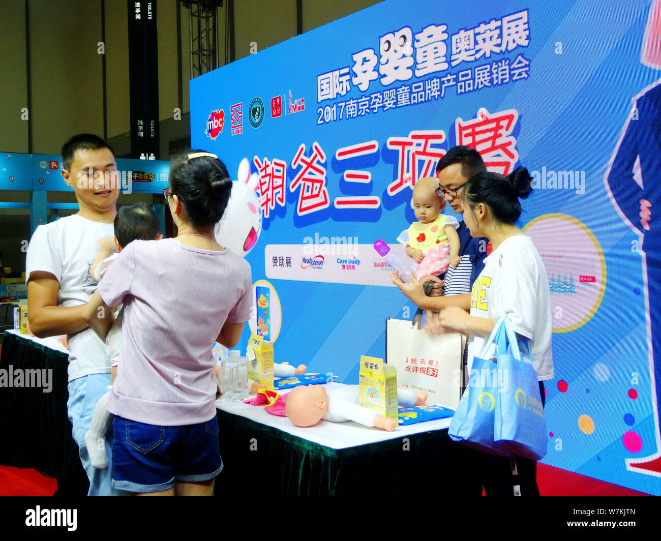 Chinese fathers-to-be and fathers try to feed babies with milk at a stand during the Nanjing Maternity-Baby-Children Brand Name Products Expo 2017 in Stock Photo