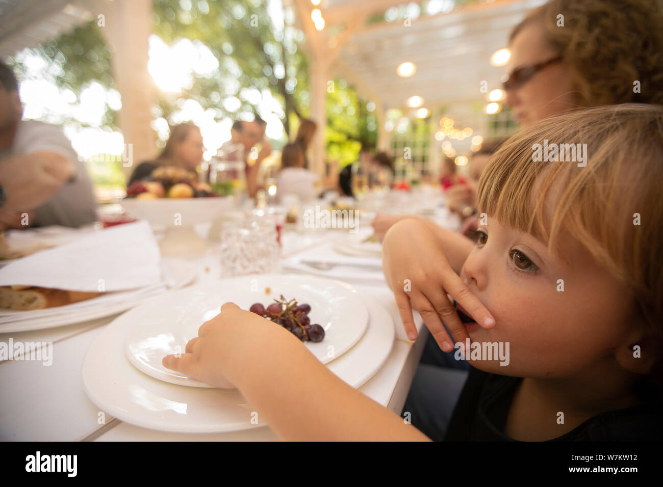 Curios kid eating grapes at table in outside restaurant Stock Photo
