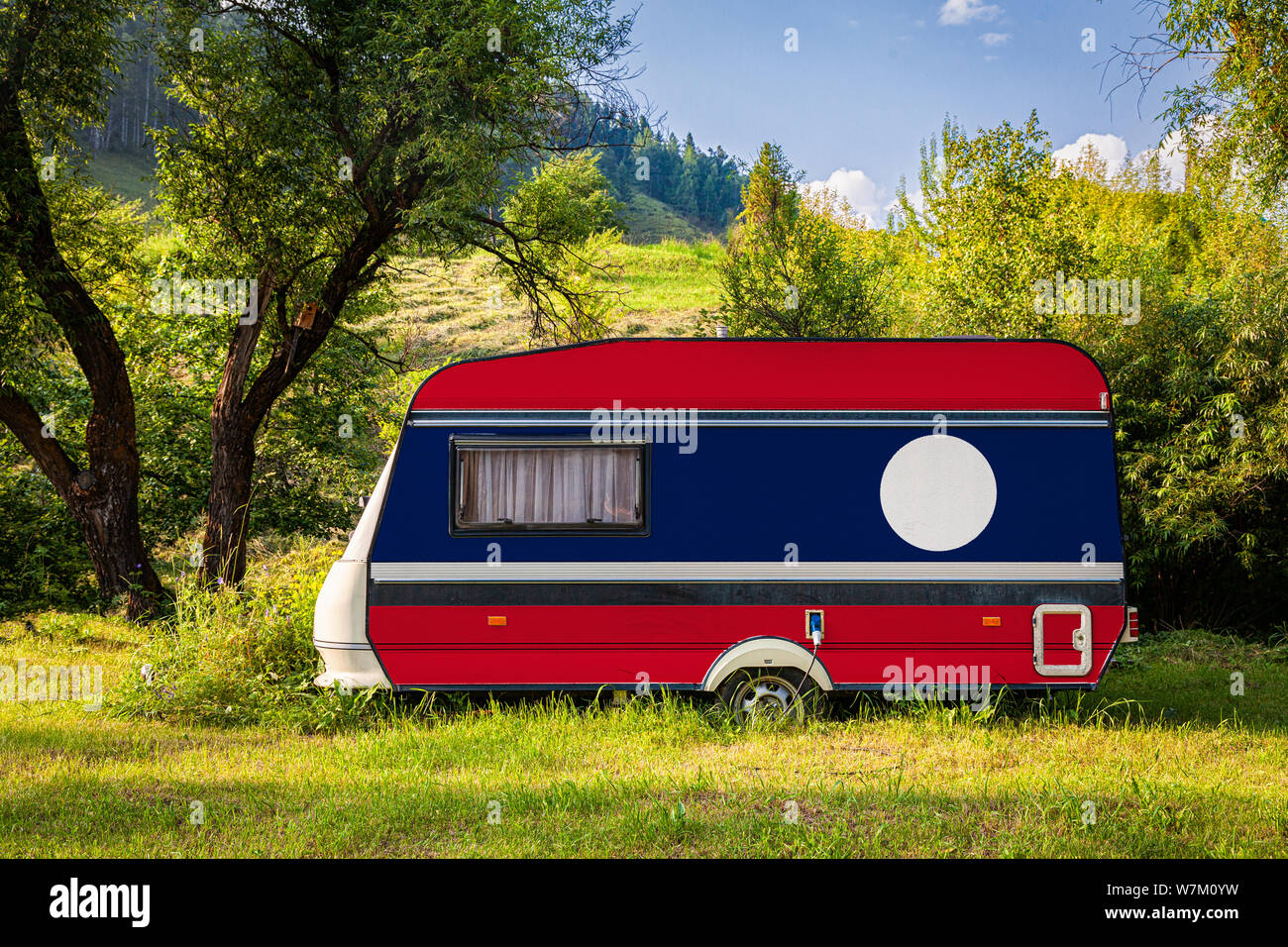 A car trailer, a motor home, painted in the national flag of Laos stands parked in a mountainous. The concept of road transport, trade, export and imp Stock Photo