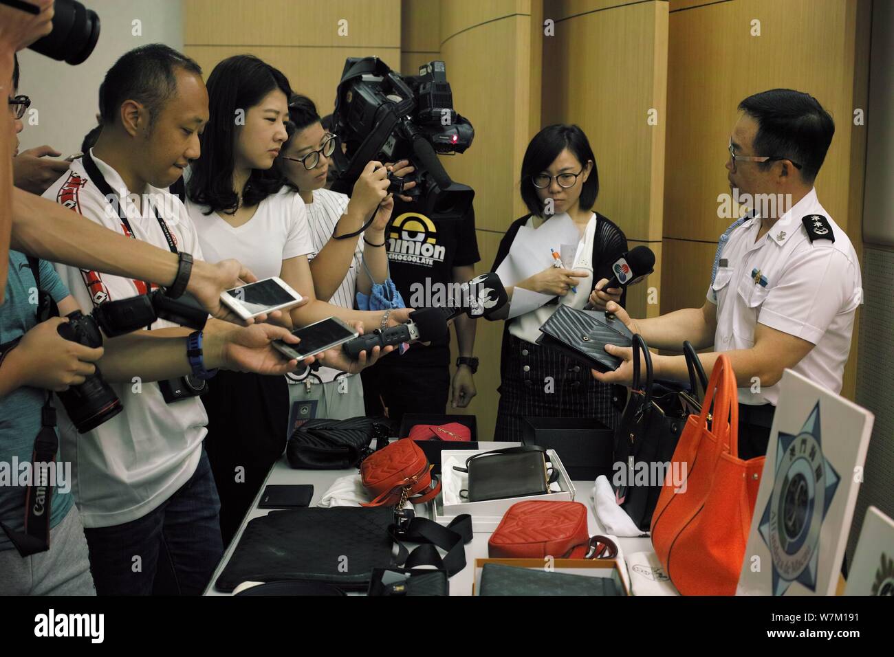 A police officer shows the fake luxury products sold by two Chinese women to customers in mainland China as he is interviewed at a police station in M Stock Photo