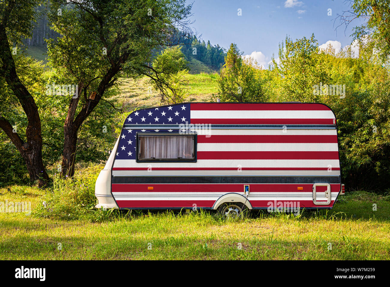 A car trailer, a motor home, painted in the national flag of  USA stands parked in a mountainous. The concept of road transport, trade, export and imp Stock Photo