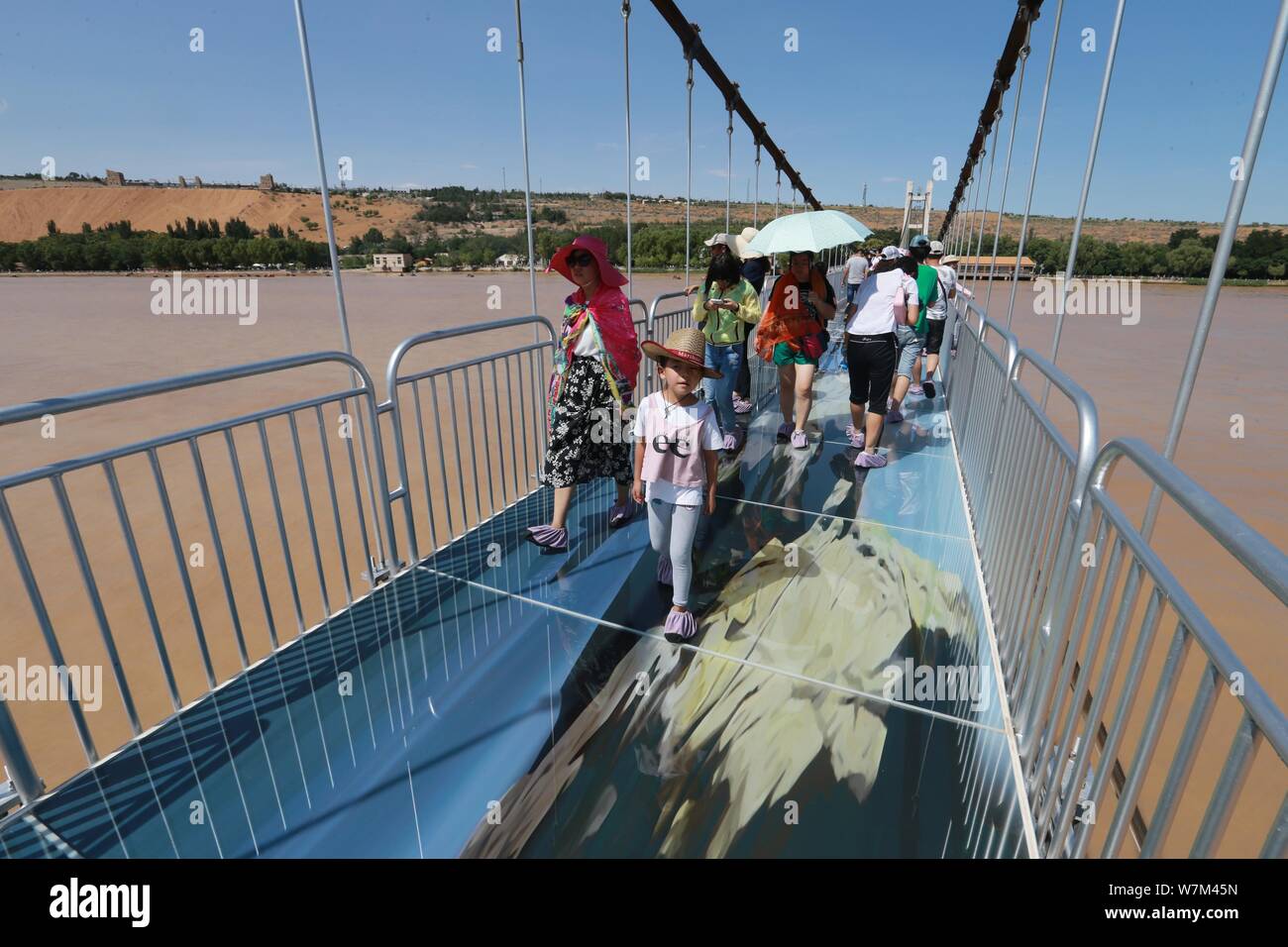 Tourists walk on the 3D glass bridge crossing over the Yellow River inside Shapotou Tourist Zone in Zhongwei city, northwest China's Ningxia Hui Auton Stock Photo