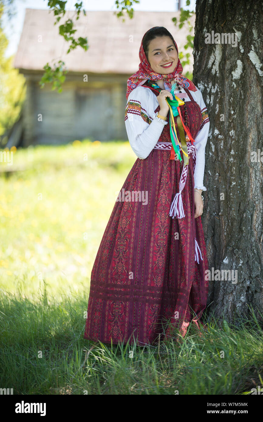 Young woman in traditional russian clothes standing under a tree