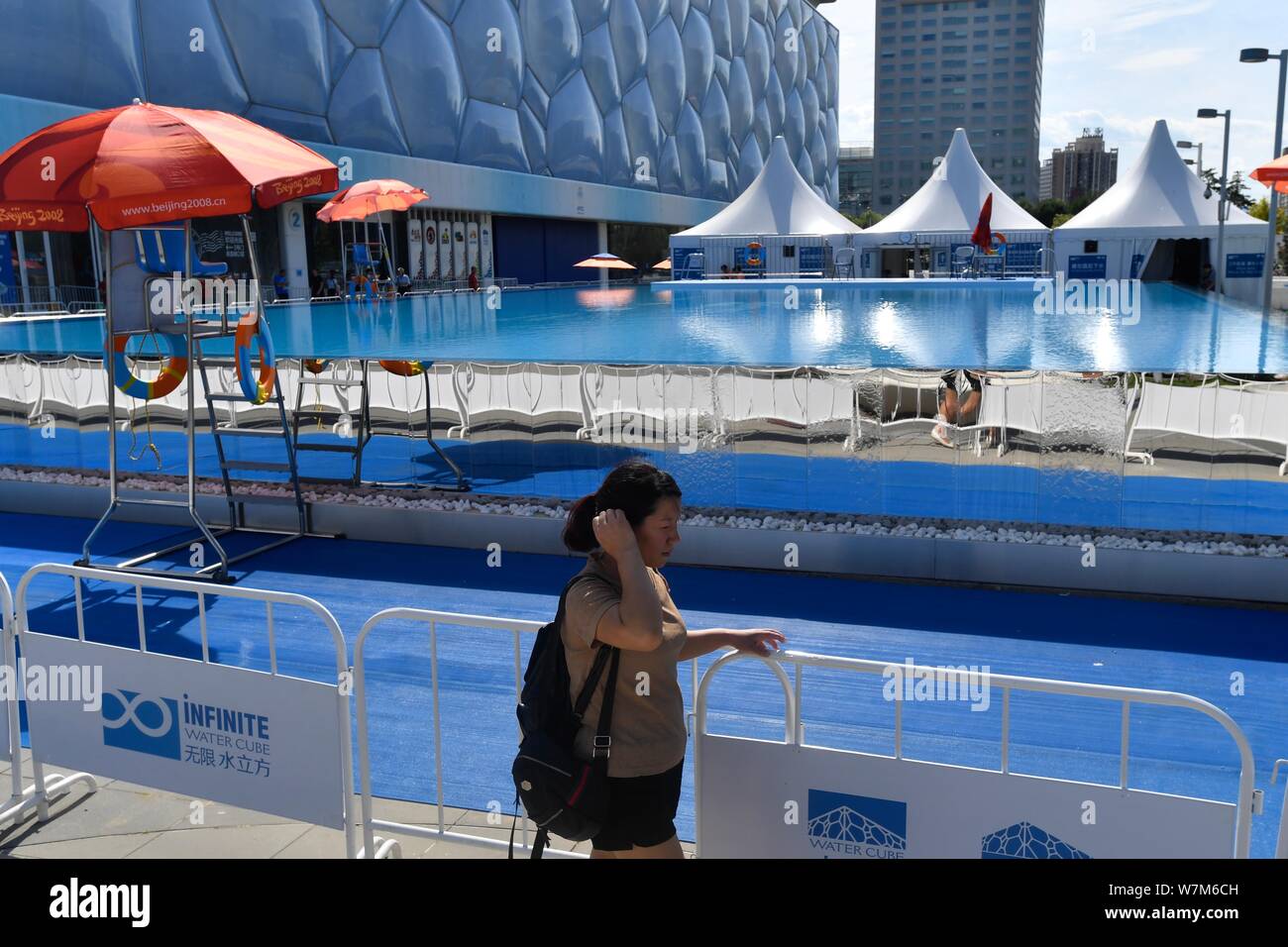 A pedestrian walks past the 25 meters long and 15 meters wide infinity pool beside China's National Aquatics Center, better known as 'Water Cube', in Stock Photo