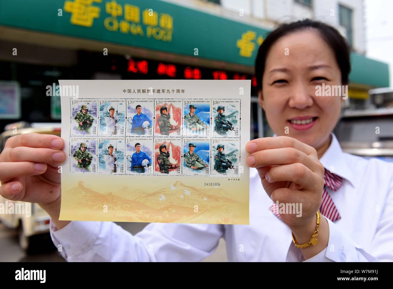 A Chinese employee shows commemorative stamps for the 90th anniversary of the founding of the Chinese People's Liberation Army (PLA) at a branch of Ch Stock Photo
