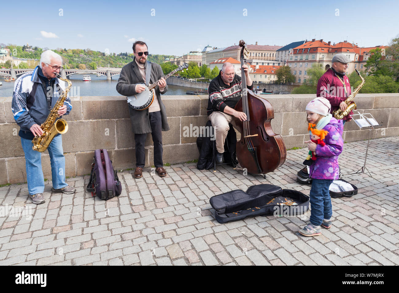 Prague, Czech Republic - April 30, 2017: Band of street musicians plays for tourists on the Charles Bridge in Prague. Little girl puts money in a guit Stock Photo