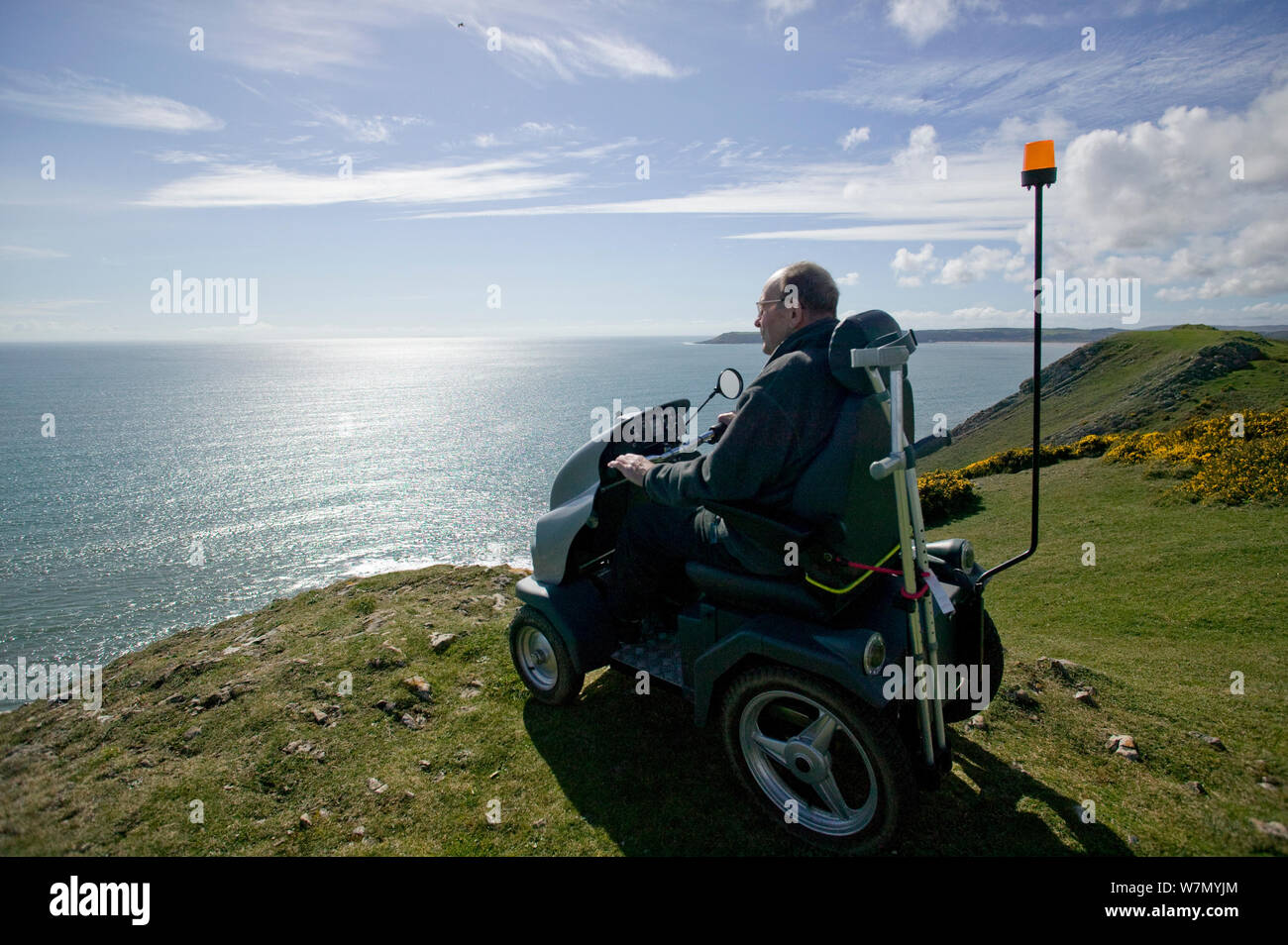 Disabled Man in his 80's enjoying stunning coastal scenery from Pennard cliff using 'Tramper ' machine designed to aid mobility to difficult places for disabled people, Gower, South Wales, UK 2009 Stock Photo