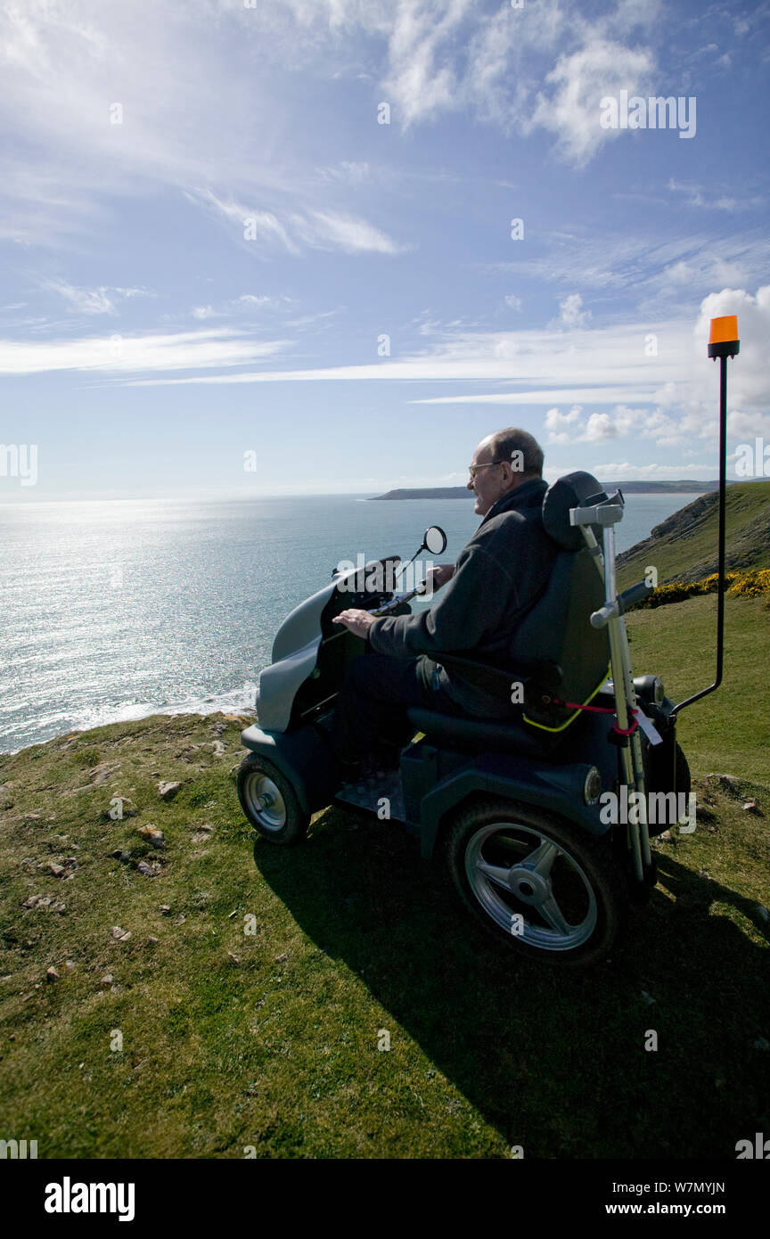 Disabled Man in his 80's enjoying stunning coastal scenery from Pennard cliff using 'Tramper ' machine designed to aid mobility to difficult places for disabled people, Gower, South Wales, UK 2009 Stock Photo