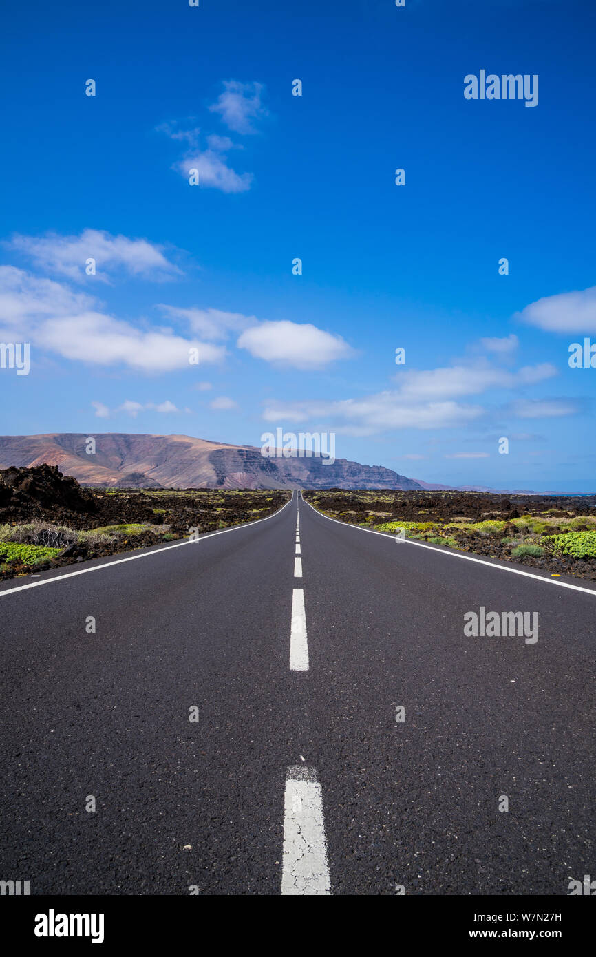 Spain, Lanzarote, Straight endless road through volcanic nature scenery under blue sky Stock Photo