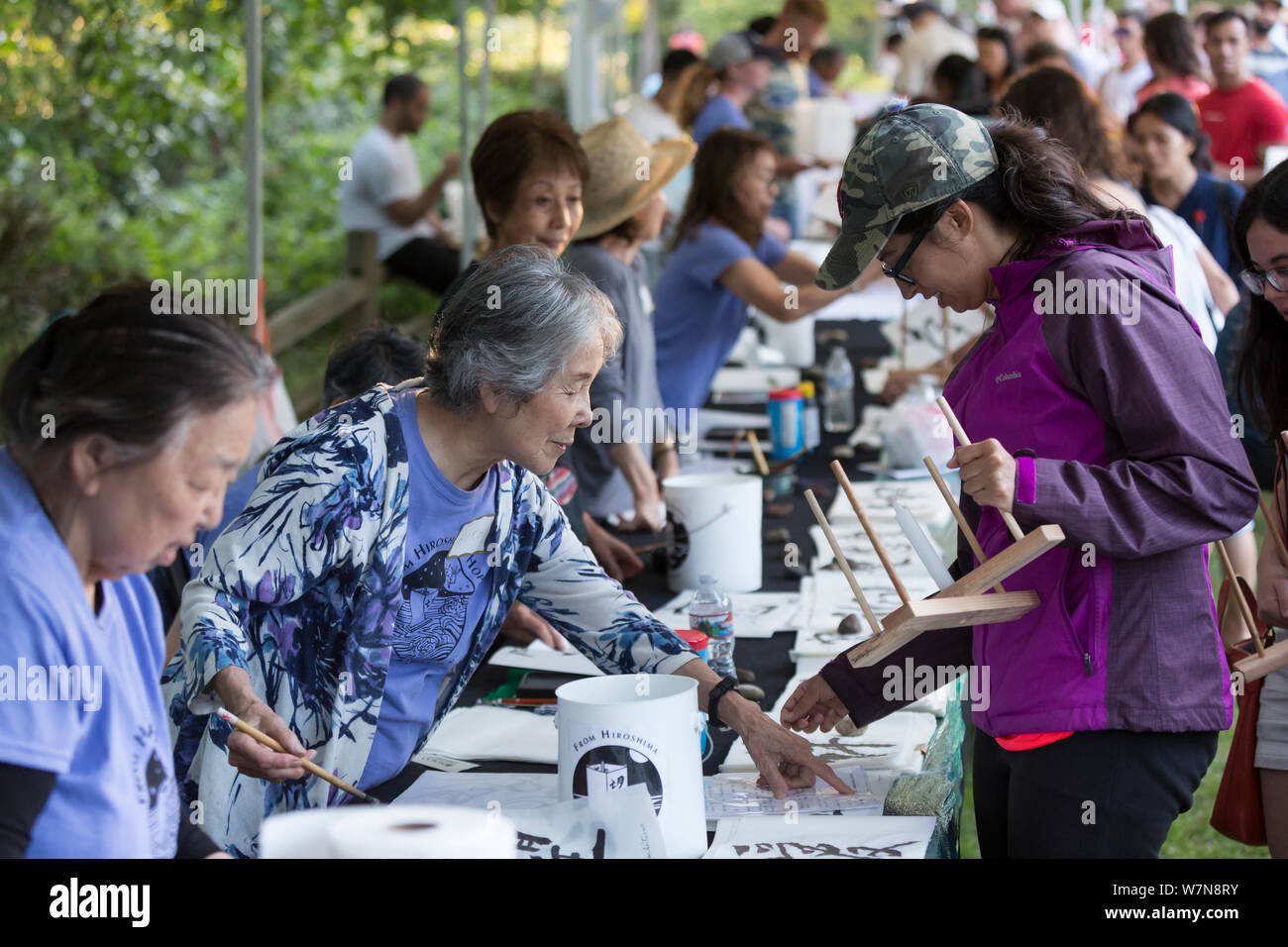 A Japanese calligrapher writes a message on a paper lantern for a women at the Toro Nagashi Lantern Floating Ceremony in Seattle, Washington on August 6, 2019. “From Hiroshima To Hope” is held in remembrance of atomic bomb victims on the anniversary of the bombing of Hiroshima, Japan. The ceremony, organized by a collation of peace, religious, civil liberties and cultural heritage organizations, honors victims of the bombings of Hiroshima and Nagasaki, and all victims of violence. It is an adaptation of an ancient Japanese Buddhist ritual, the Toro Nagashi, in which lanterns representing the s Stock Photo