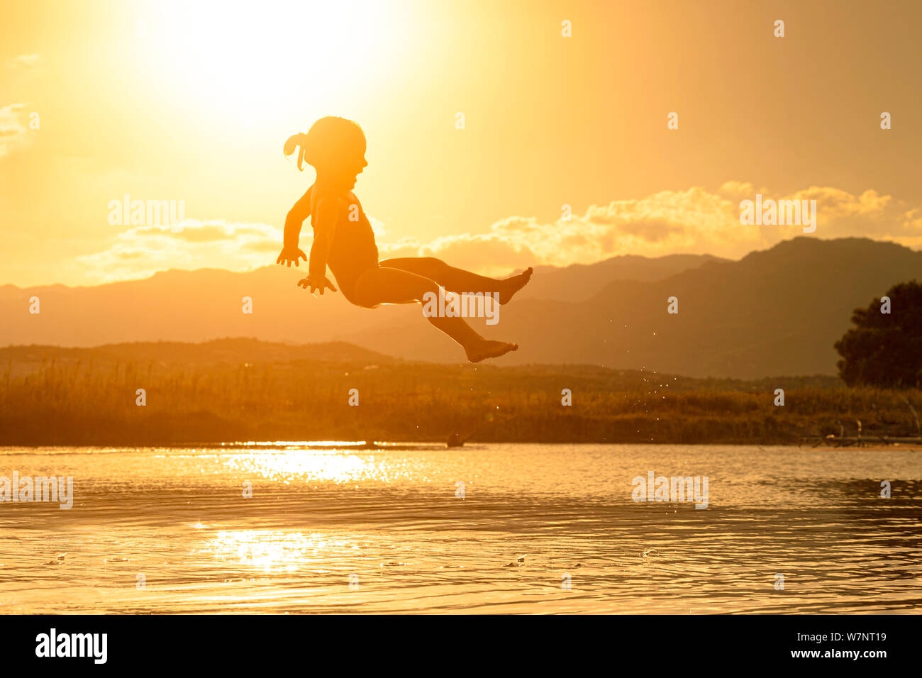 3 year old girl jumps into the sea at sunset. carefree and happy concept Stock Photo