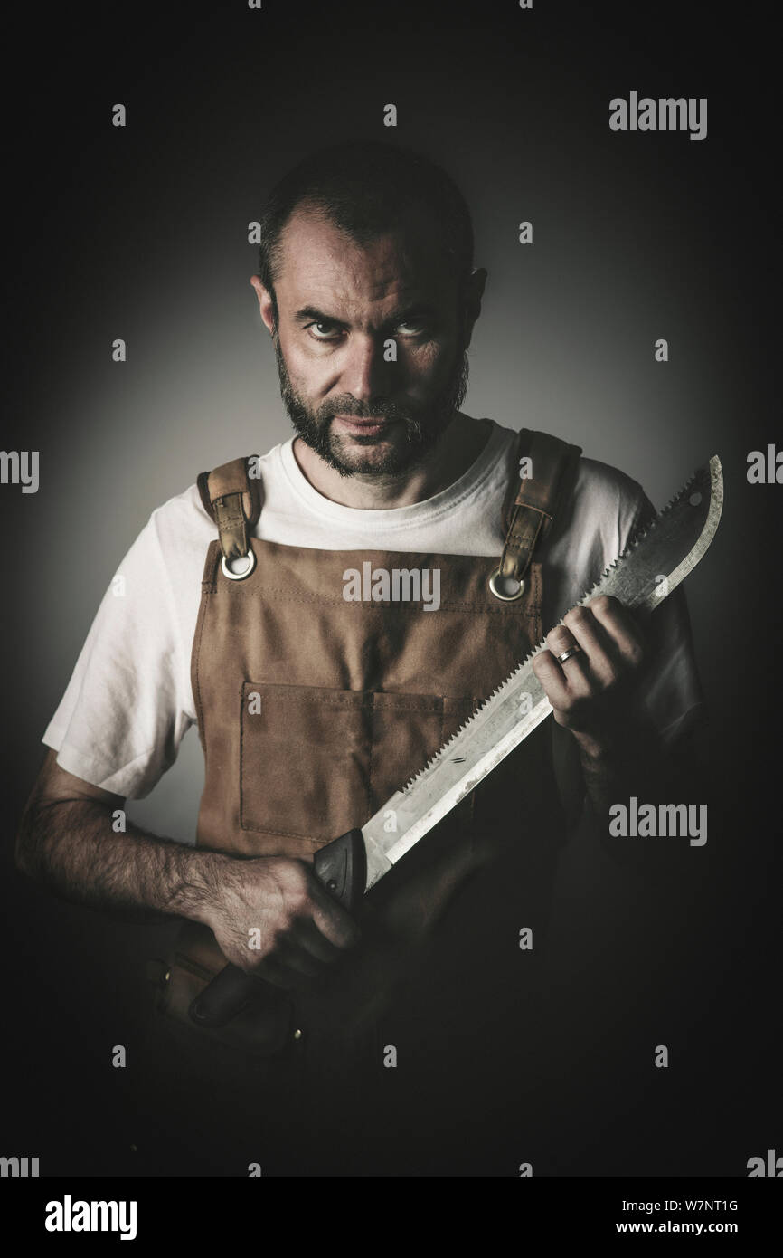 dramatic portrait of a killer holding a machete, concept of danger and image suitable for the horror theme. Stock Photo