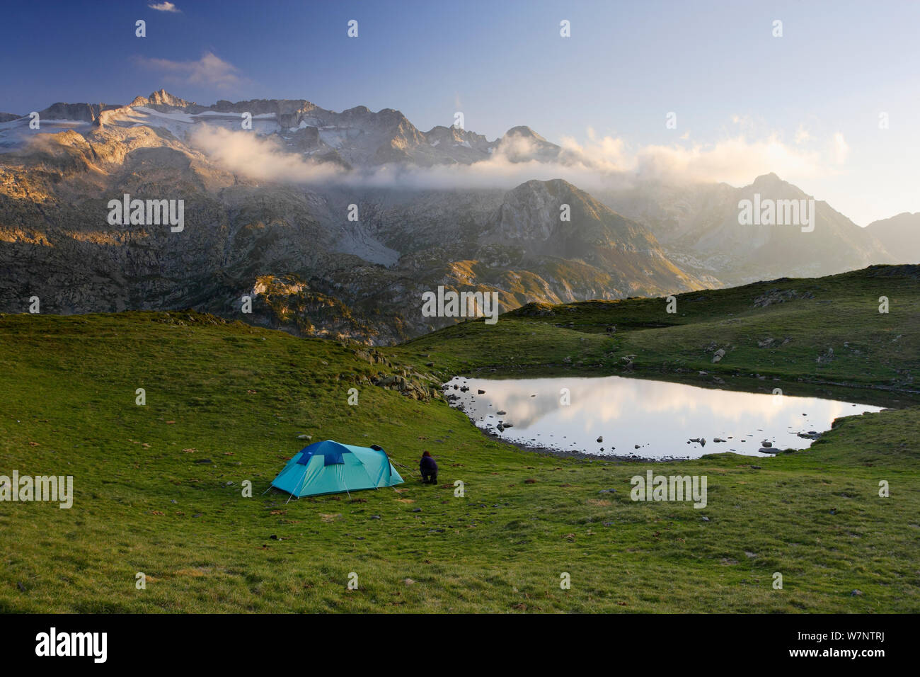 Mountaineer setting up camp below La Picada pass, with Aneto (3404 m) and Maladeta (3308 m) peaks with its glaciers in the massif of Maladeta in the background, Posets-Maladeta Natural Park, Pyrenees, Aragon, Spain Stock Photo