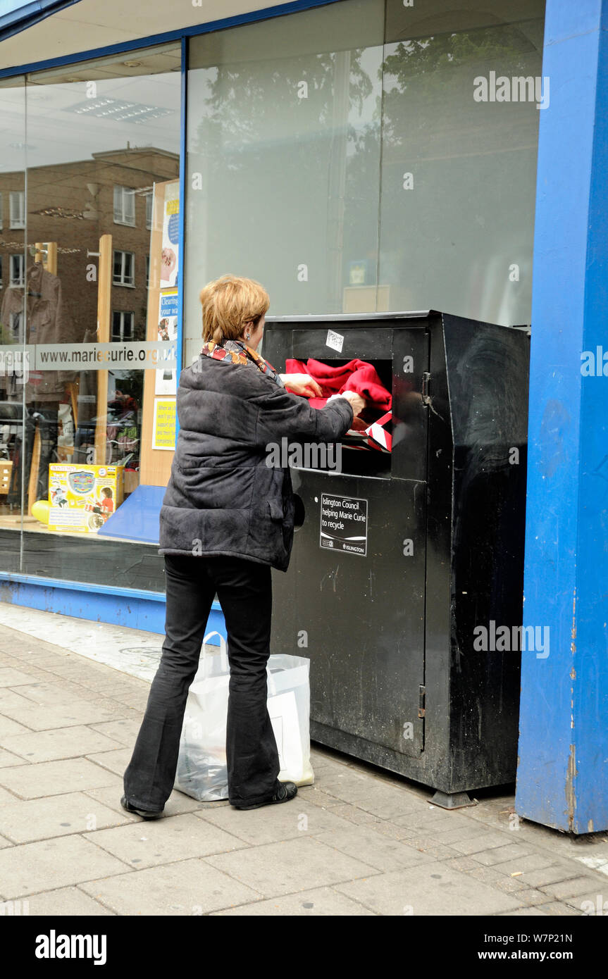 Woman recycling clothes into a clothes bank outside a charity shop