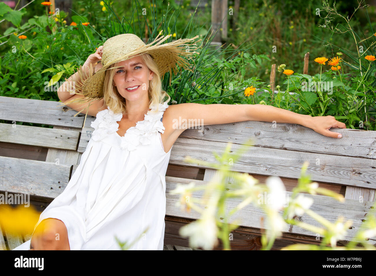 beautiful blonde woman in white dress and straw hat sitting outside in ...
