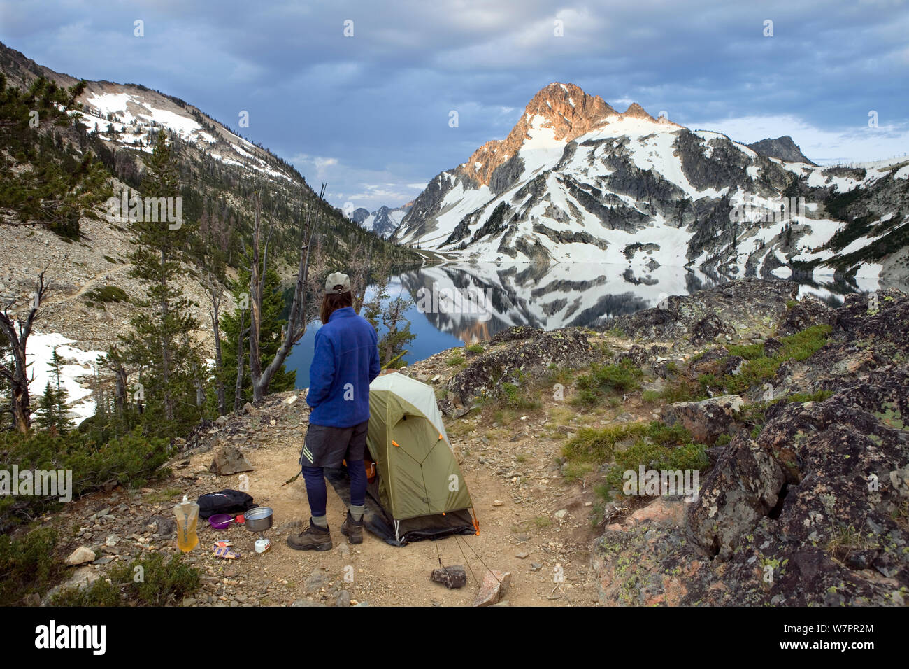Hiker standing beside tent above Sawtooth Lake with  Mount Regan behind in the Sawtooth Wilderness. Idaho, USA. Model released. Stock Photo