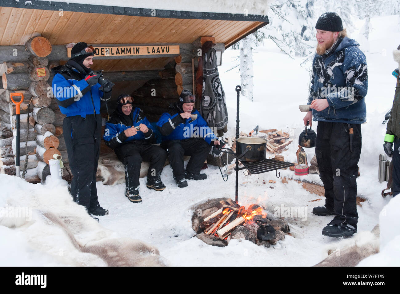 Tourists take lunch break round fire after Dog-sledding inside Riisitunturi National Park, Lapland, Finland Stock Photo