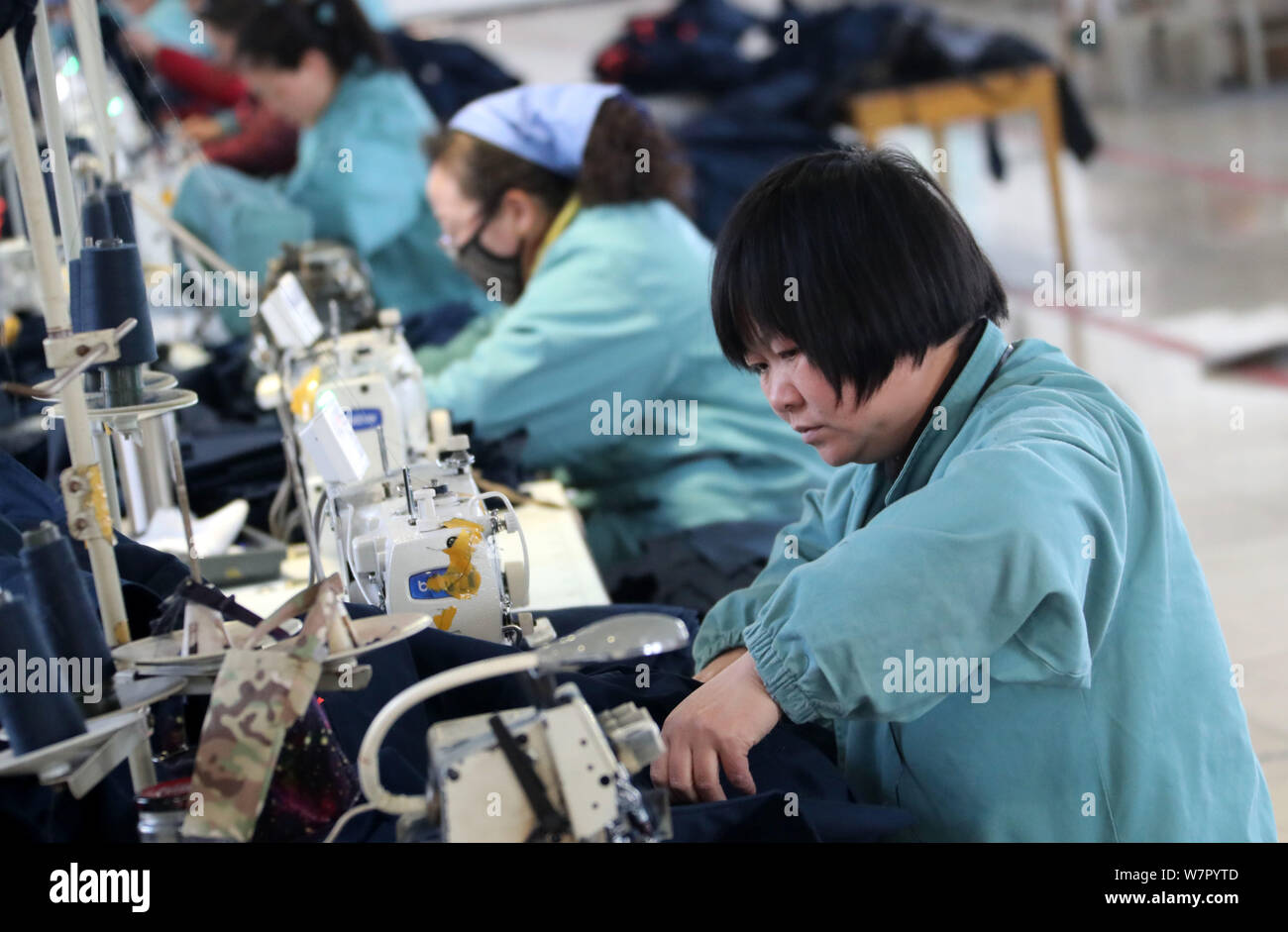 Female Chinese workers sew clothes to be exported to Southeast Asia on a spinning machine at a textile factory in Huaibei city, east China's Anhui pro Stock Photo