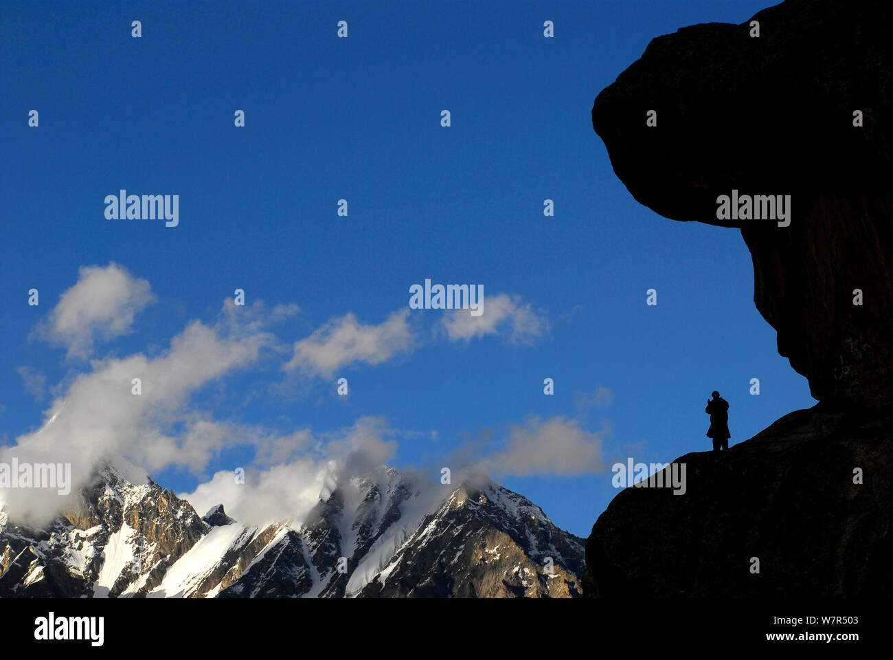 A Balti porter silhouetted standing on a rock, with mountains in the distance, Urdukas Camp (4,000m), Baltoro Glacier, Central Karakoram National Park, Pakistan, July 2007. Stock Photo