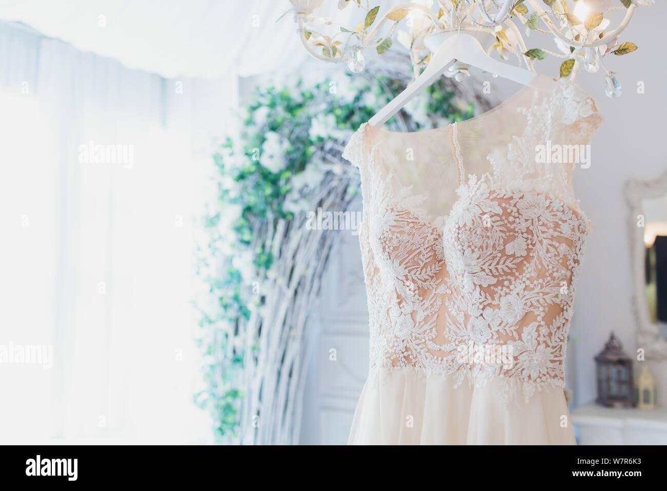 Rich Pink Wedding Dress Hangs On A Chandelier In A White Room