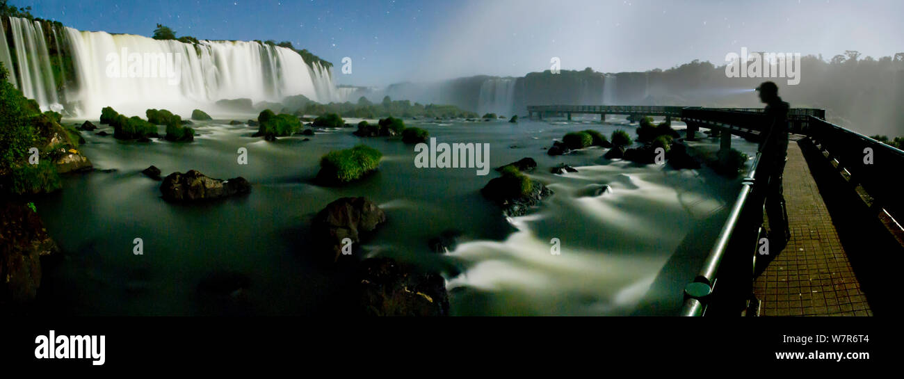 Tourist looking at Iguazu Falls by moonlight  on the Iguasu River, Brazil / Argentina border. Photographed from the Brazilian side of the Falls. State of Parana, Brazil. Stock Photo