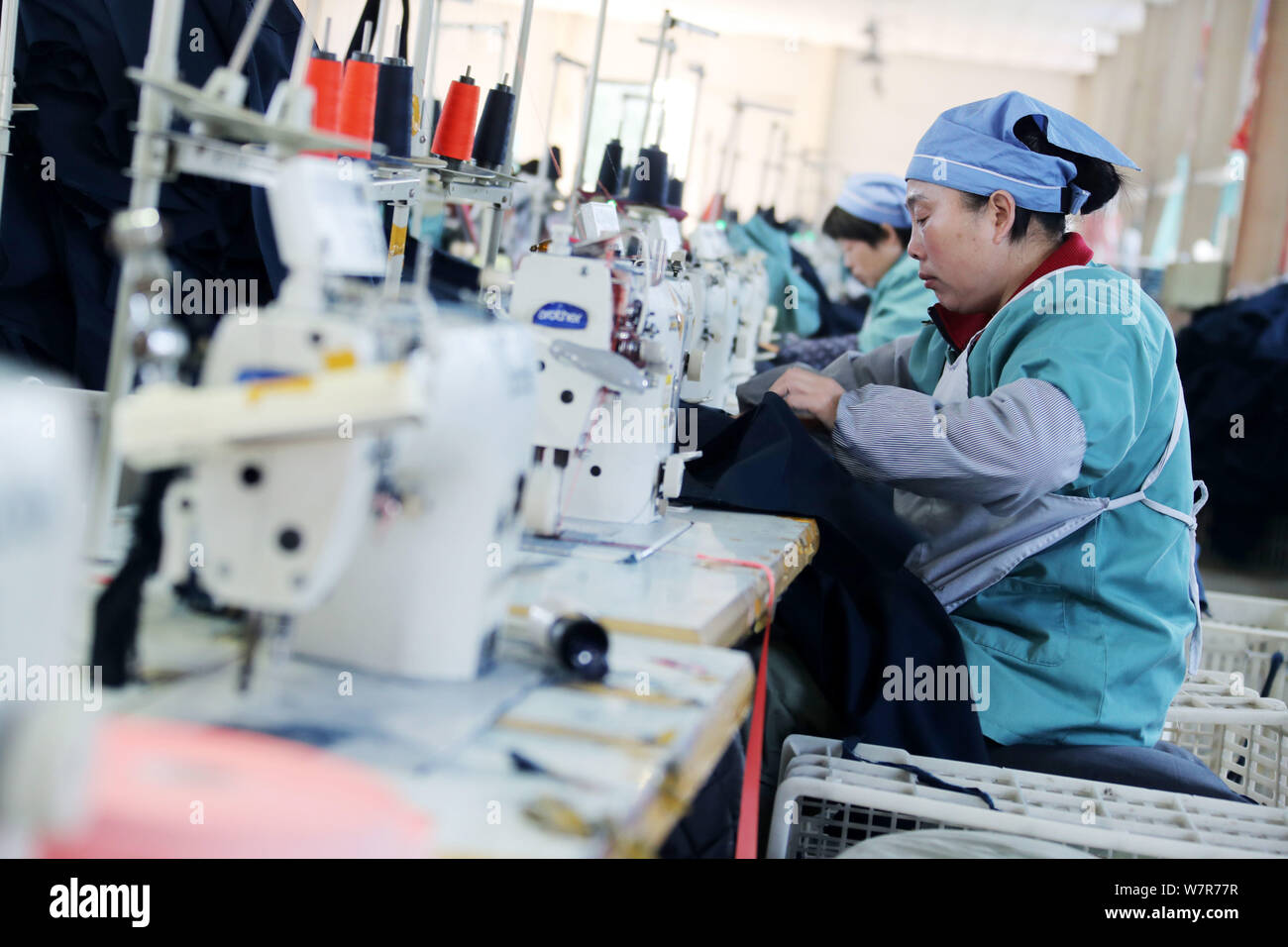Female Chinese workers sew clothes to be exported to Southeast Asia on a spinning machine at a textile factory in Huaibei city, east China's Anhui pro Stock Photo