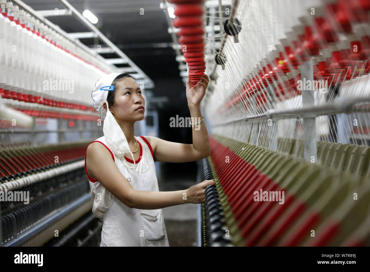 A female Chinese worker handles production of yarn to be exported to Southeast Asia on a spinning machine at a textile factory in Huaibei city, east C Stock Photo