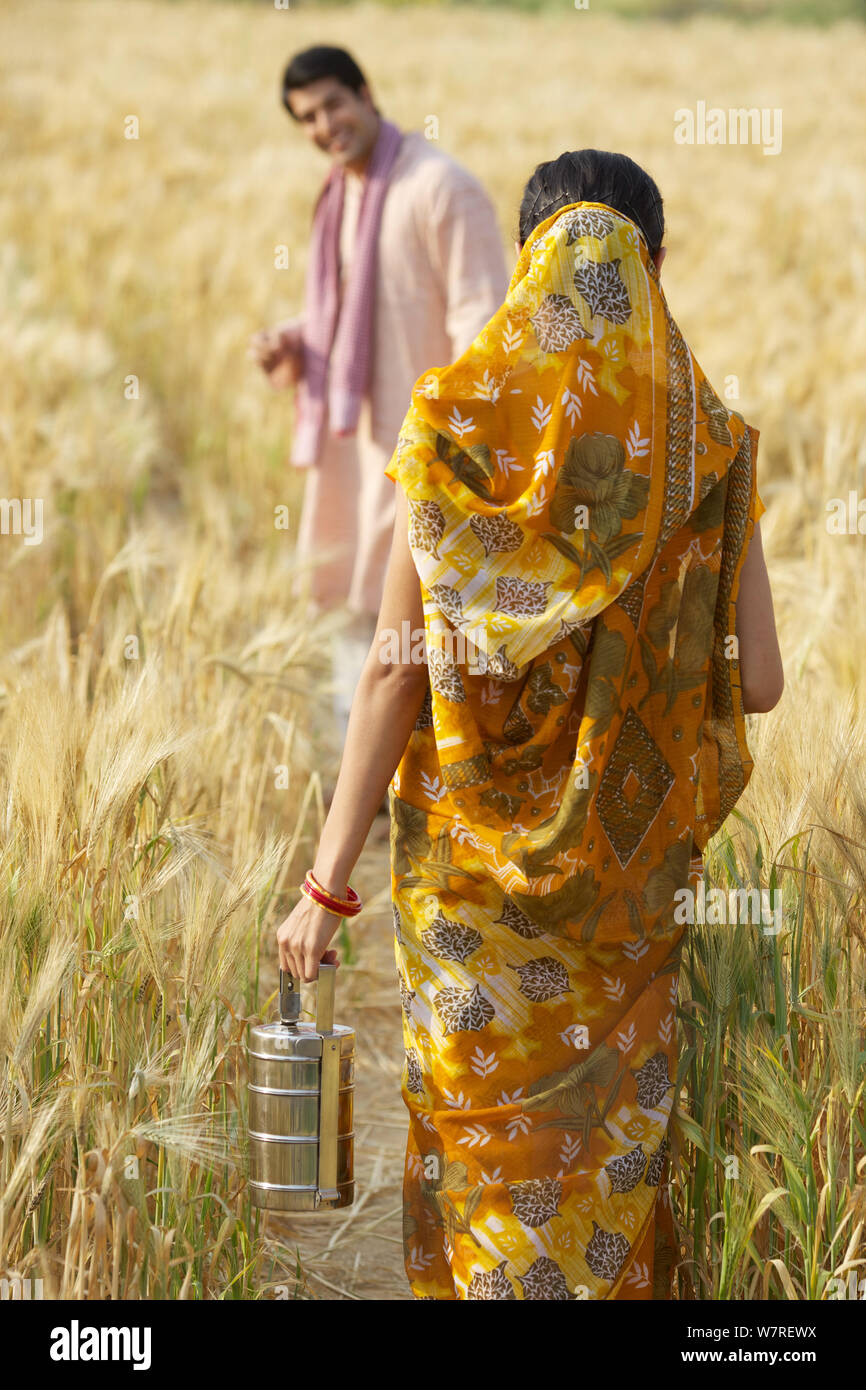 Farmer working in agriculture field and his wife walking with lunch ...