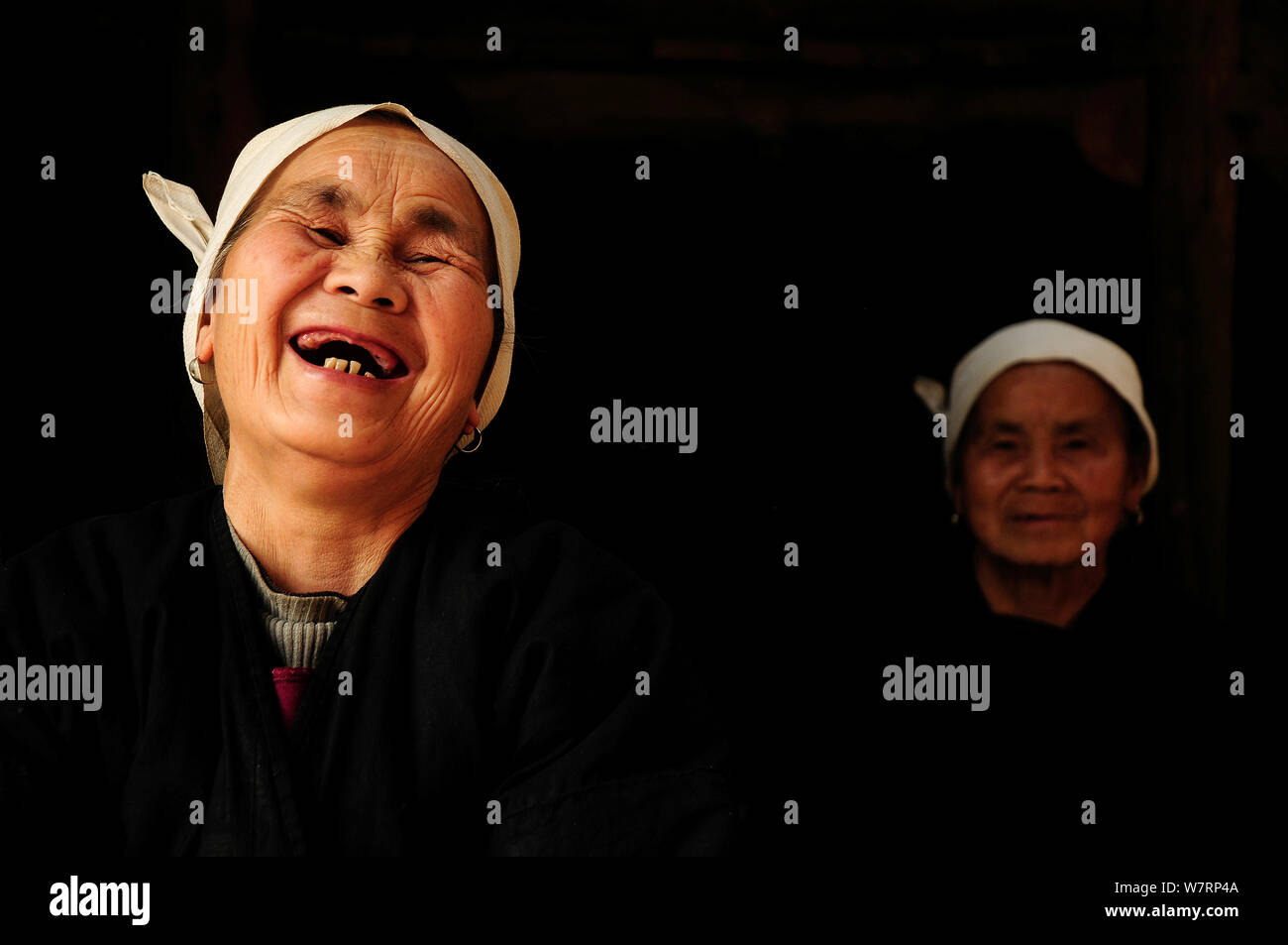 Two Dong women, one laughing, in a dark room, Sanjiang Dong Village in the province of Guangxi, China. April 2009. Winner of the Photographer of the Year, Portrait Category, 4th Pollux Awards, 2012 Stock Photo
