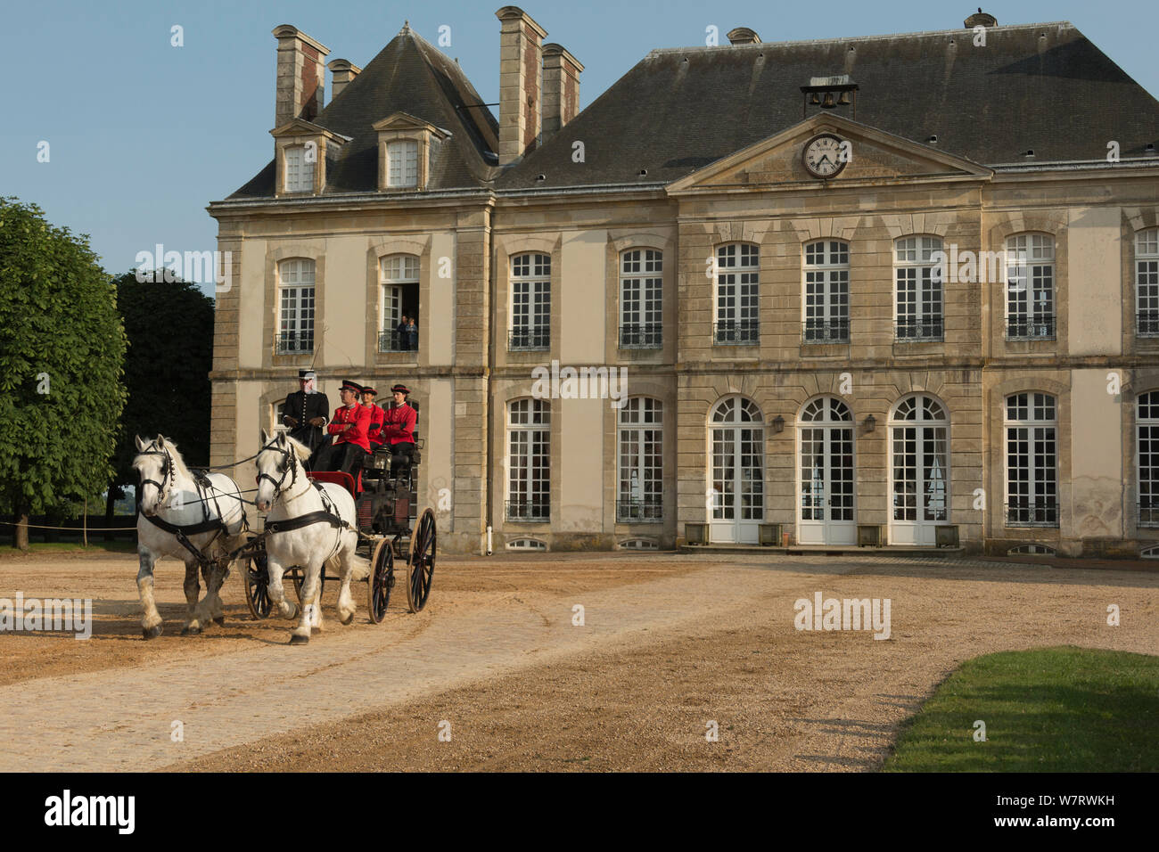The drivingr (in black) and grooms (in red) from the Haras Du Pin, France's oldest national stud, driving two Percheron horses, harnessed to a break, in the Cour D'Honneur, at Le Pin-au-Haras, Orne, Lower Normandy, France. July 2013 Stock Photo