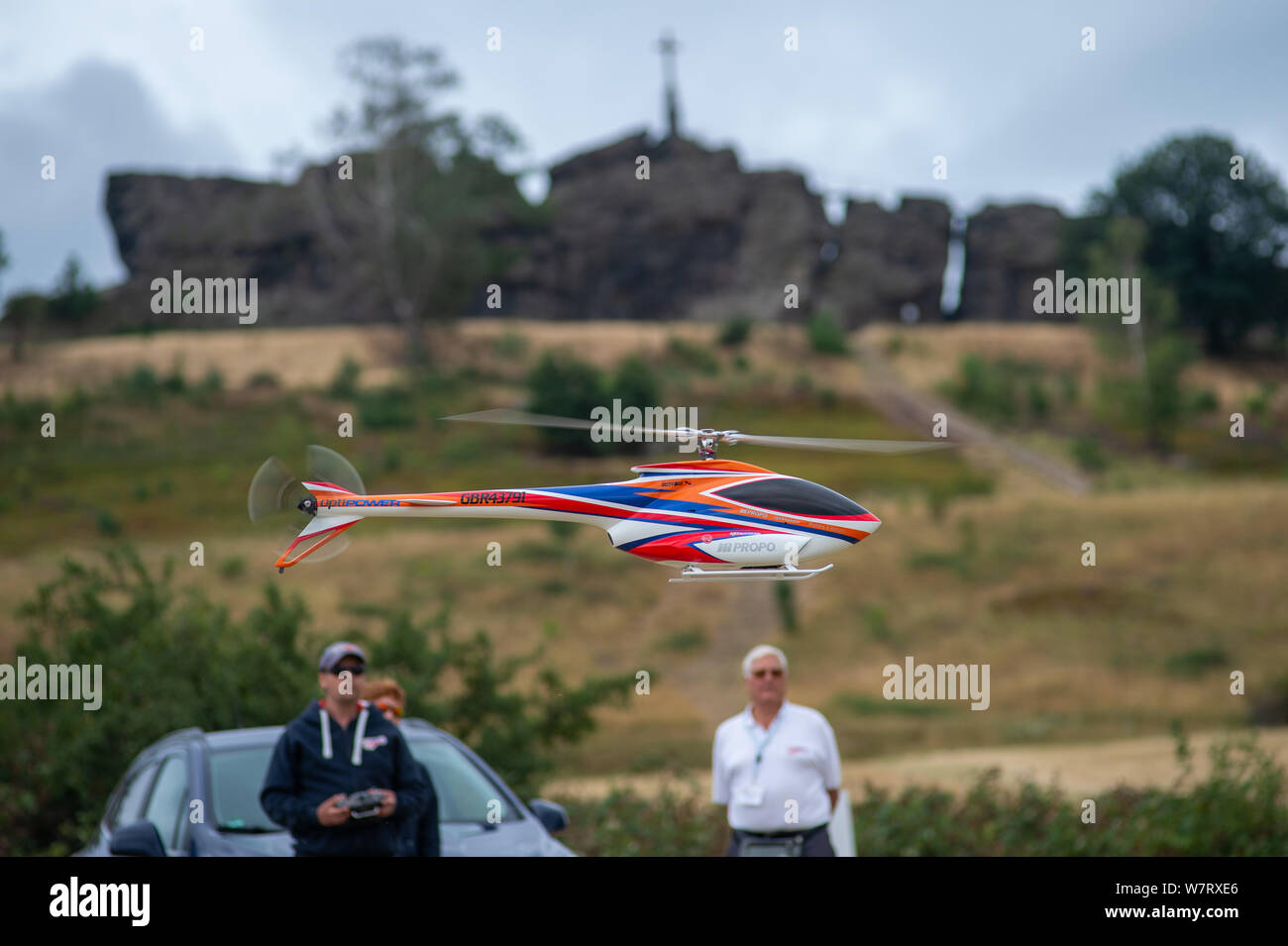 07 August 2019, Saxony-Anhalt, Ballenstedt: Stephen Roberts (l) from Team  Great Britain starts his model helicopter type Japan Radio 05. In the  background you can see the Gegensteine, a rock formation that