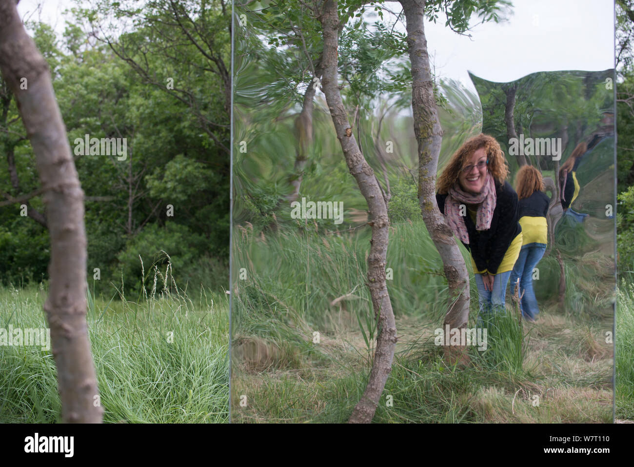 Woman looking into giant 'funhouse' mirror in forest, public sculpture by Rob Mullholland, Port saint Louis du Rhone, Camargue, France, May 2013. Editorial Use only. Credit Jean Roche / Le Citron Jaune / Mullholland Stock Photo