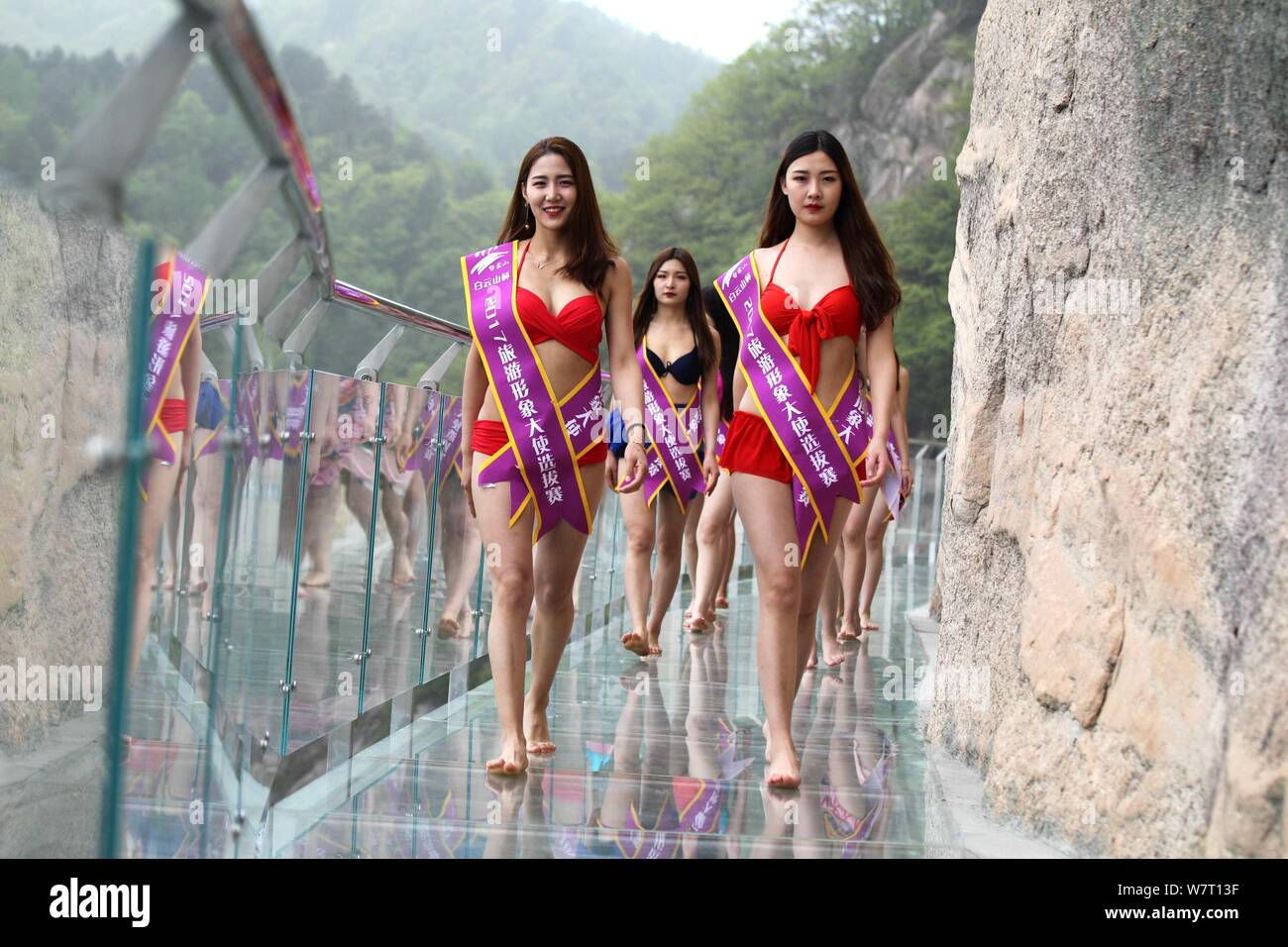 Bikini-dressed girls walk on a glass walkway along the edge of a  image