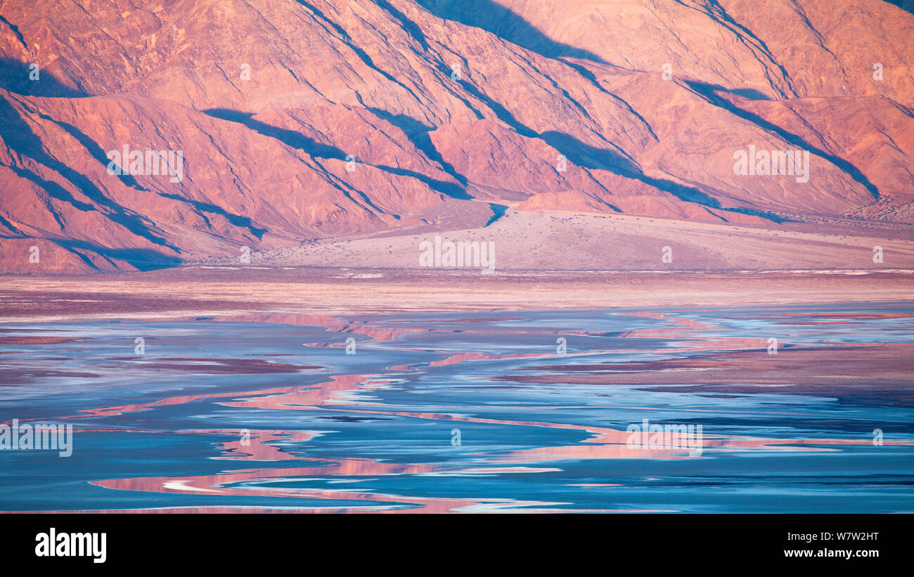 Early morning over distant mountains, creating vibrant reflections in the salt flats of Death Valley National Park, California, USA, December 2013. Stock Photo