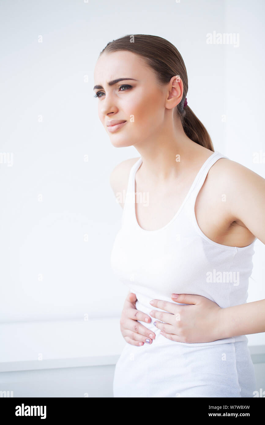 Stomach Pain. Unhealthy young woman with stomachache leaning on the bed