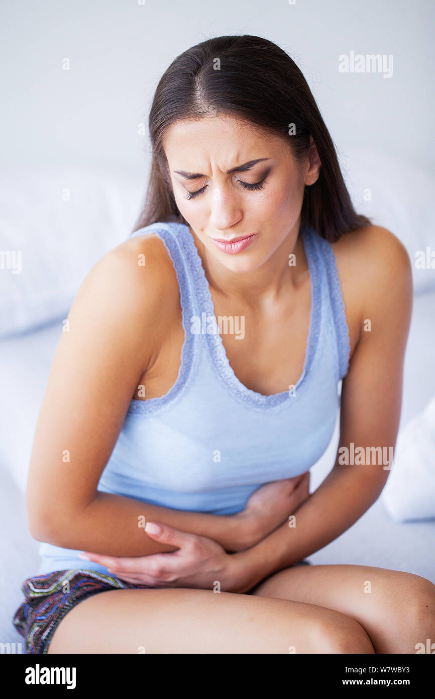 Stomach Pain. Unhealthy young woman with stomachache leaning on the bed