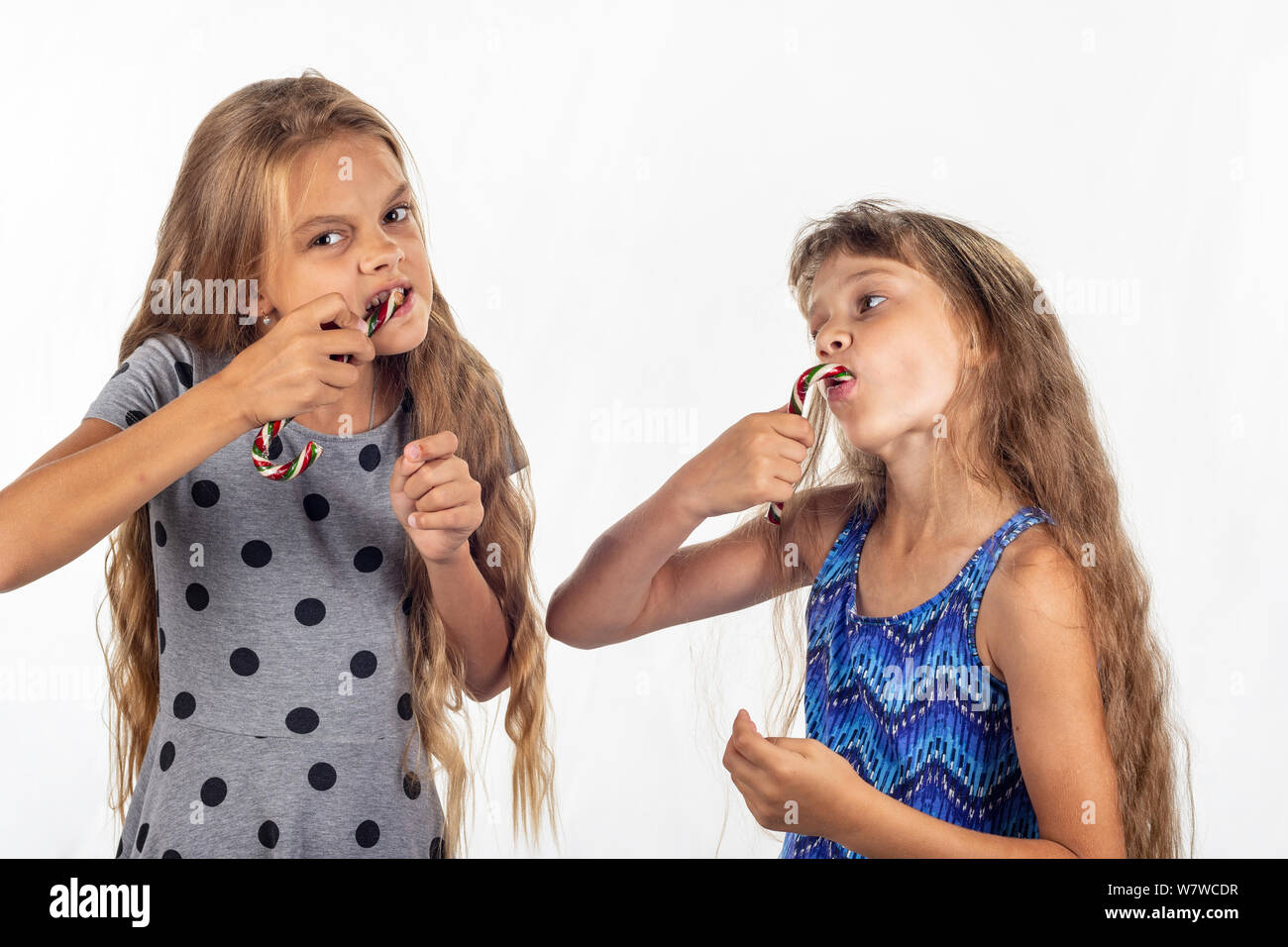 Two girls eagerly bite and suck caramel candies Stock Photo