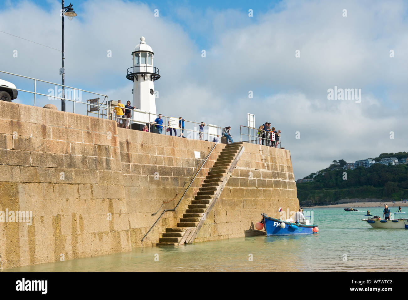 Small fishing boat next to St Ives pier and lighthouse. St Ives, Cornwall, England, United Kingdom Stock Photo