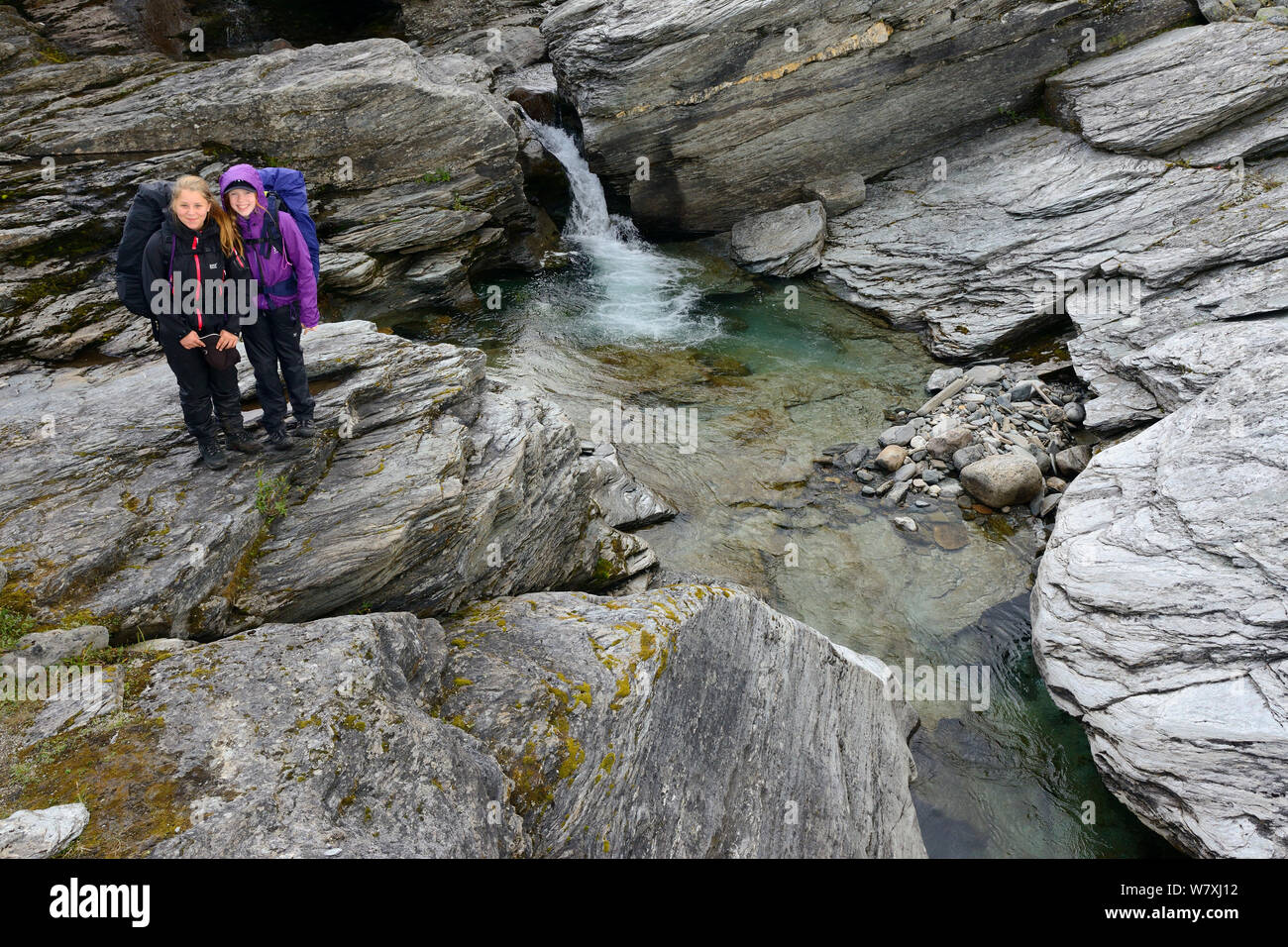 Two teenage girls standing by waterfall, on family hiking trip. Laponia Circuit, along the Padjelantaleden trail, Padjelanta National Park and Sarek National Park, Norrbotten, Lapland, Sweden. Model released Stock Photo