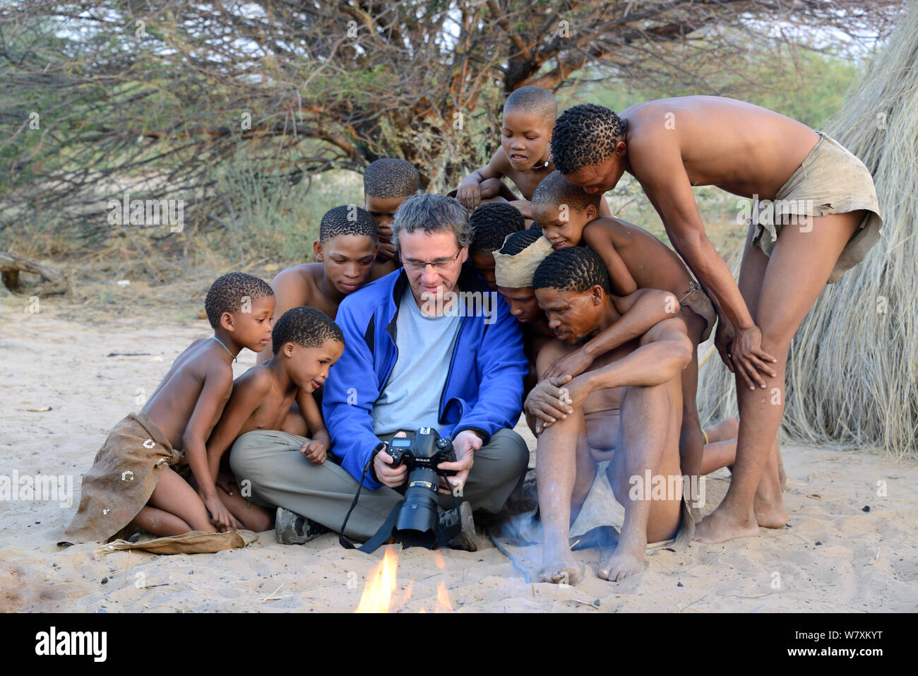 Photographer Eric Baccega showing pictures to Naro San Bushmen family with children wearing traditional clothing made with duiker leather. Kalahari, Ghanzi region, Botswana, Africa. Dry season, October 2014. Stock Photo
