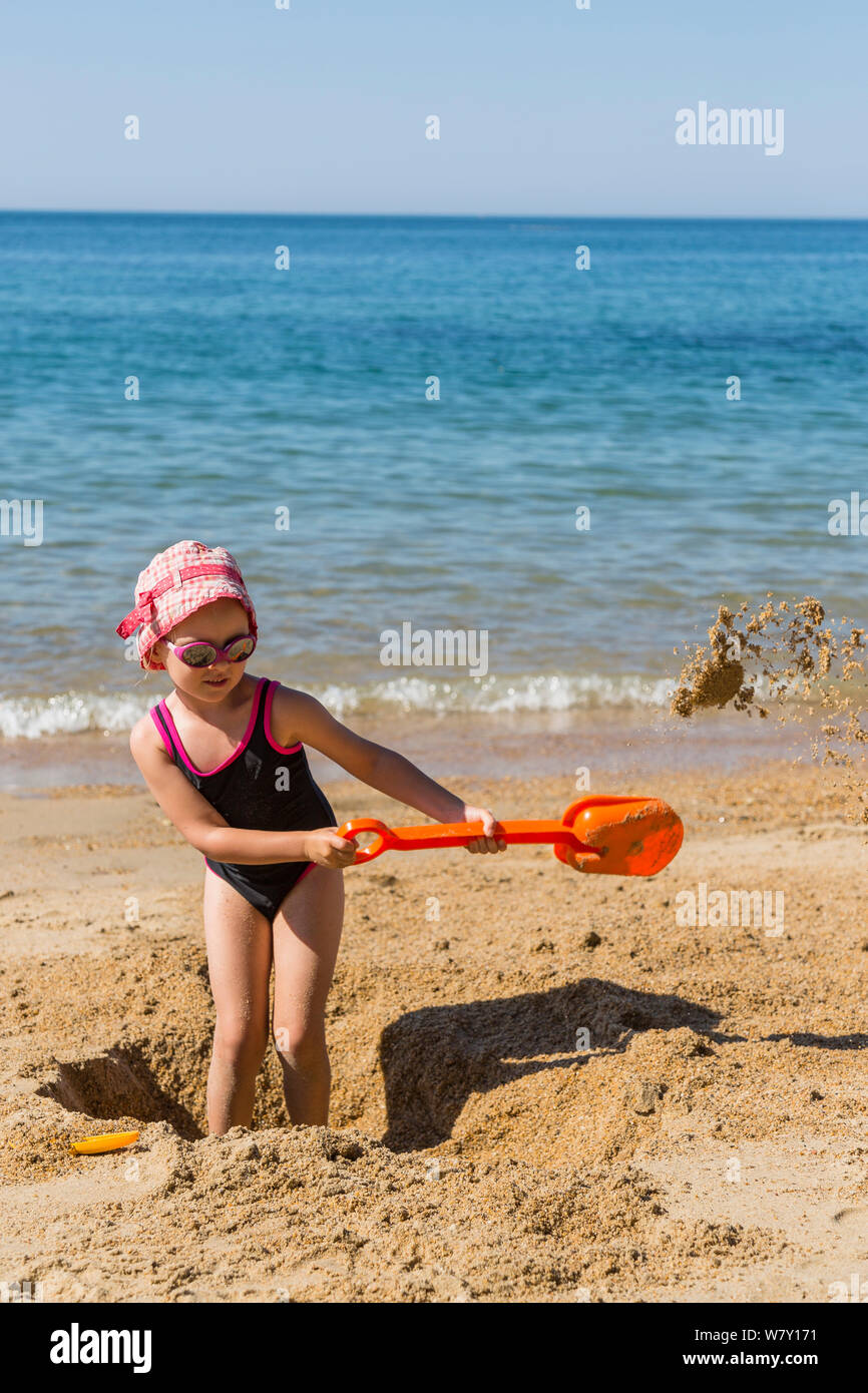 Young girl with plastic spade digging hole on the beach. Biarritz, Aquitaine, France, September 2014. Model released. Stock Photo