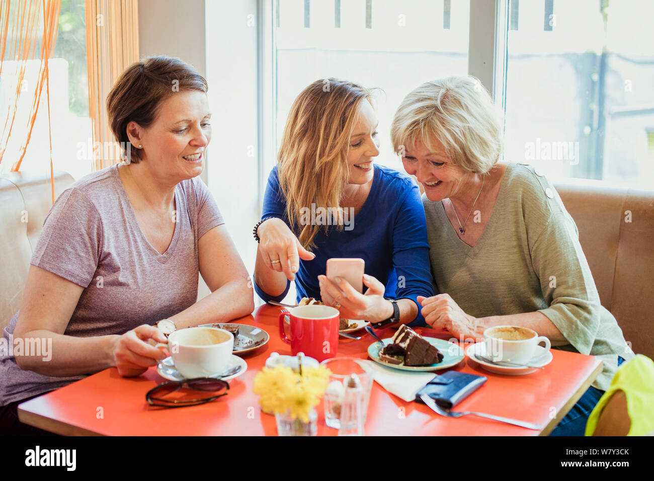 A group of three mature women having coffee and cake; they are looking at one of their phones. Stock Photo