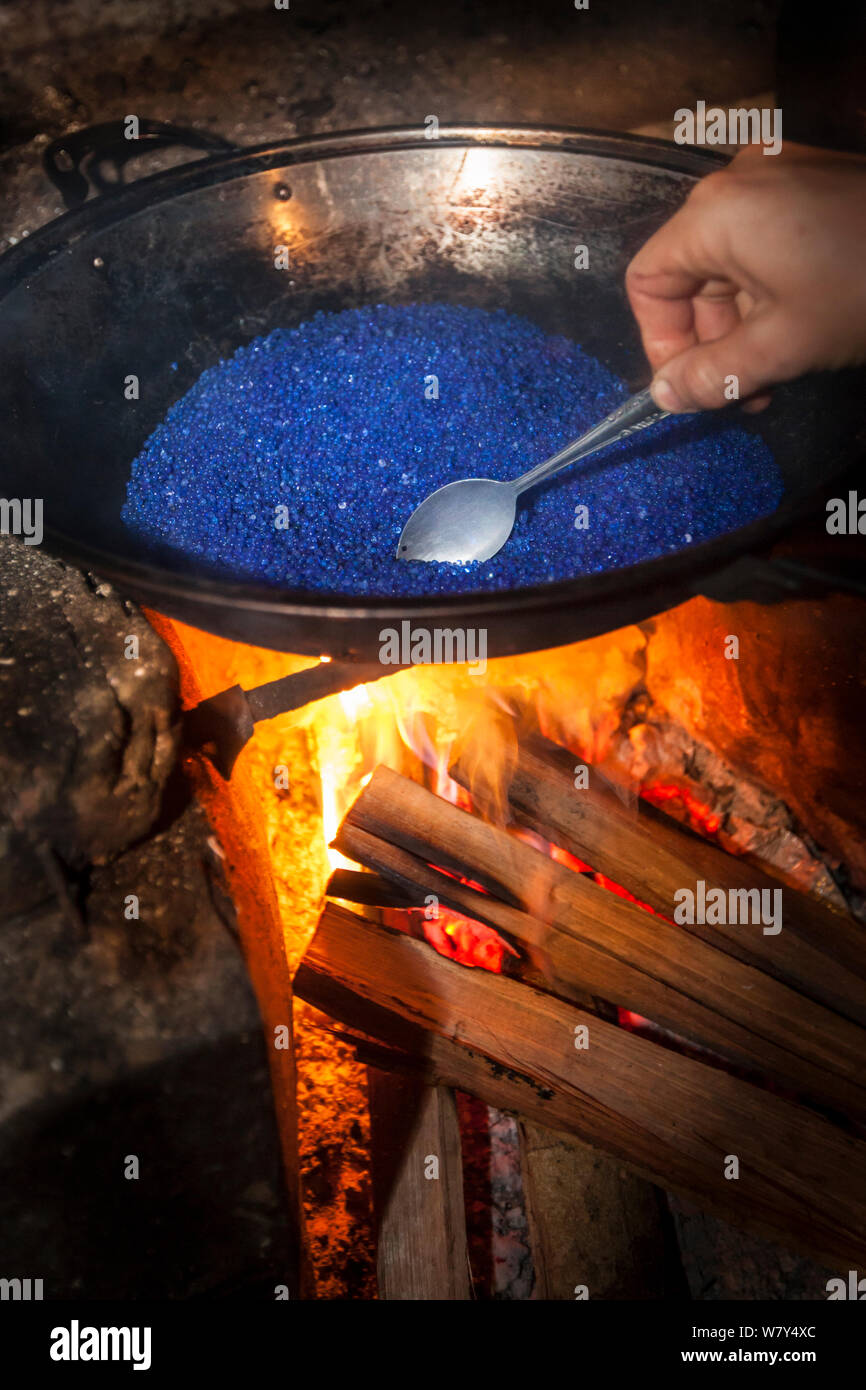 Photographer heating silica gel over camp fire in rainforest to restore its desiccating properties. The high humidity of the rainforest can fog camera lenses and lead to mould growth, so silica gel is used to trap moisture. Maliau Basin, Sabah, Borneo, May 2011. Stock Photo
