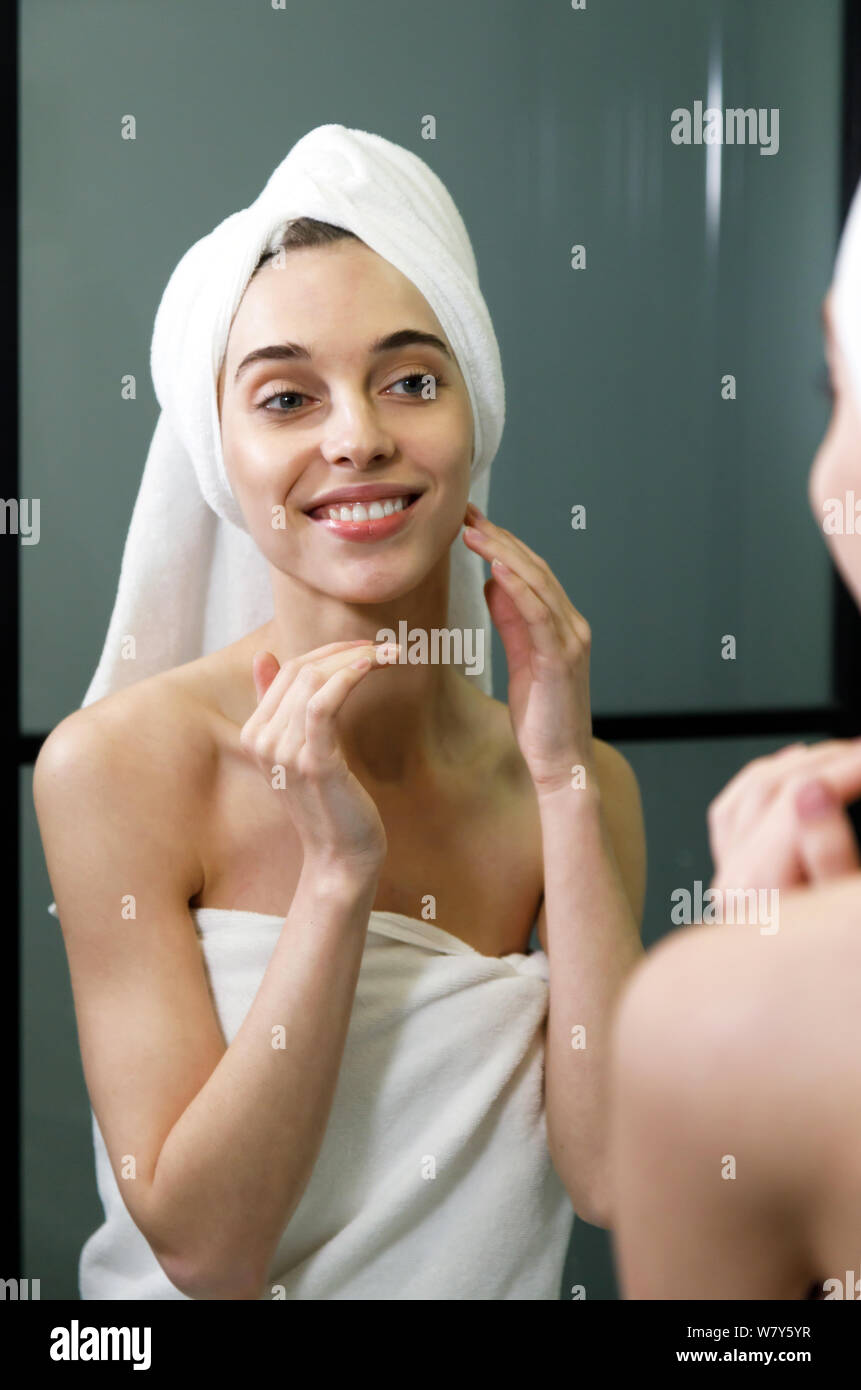 Portrait of woman wearing bath towel applying moisturizing cream near the mirror in bathroom Stock Photo