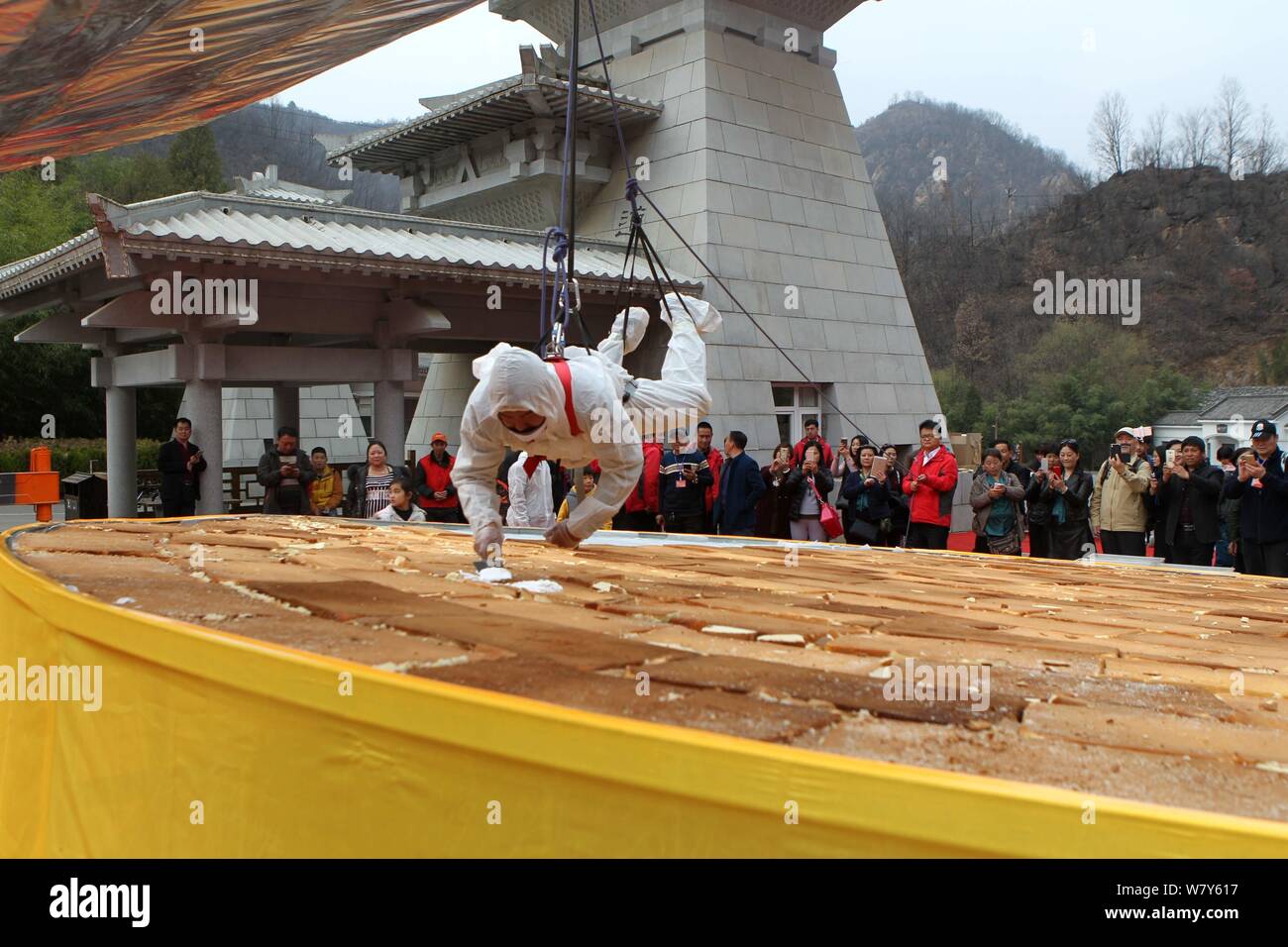 A Chinese baker lifted by a crane pastes the cream on top of a giant cake to celebrate the 2,588th birthday of the founder of Taoism Lao Zi (Laozi) on Stock Photo