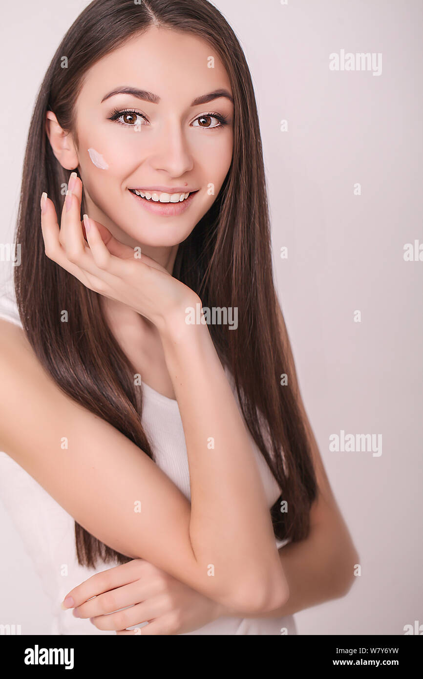 Face Treatment. Woman in Beauty Salon. Applying cosmetic cream. A beautiful young woman applying face moisturizer. Scine care of the face and hands Stock Photo