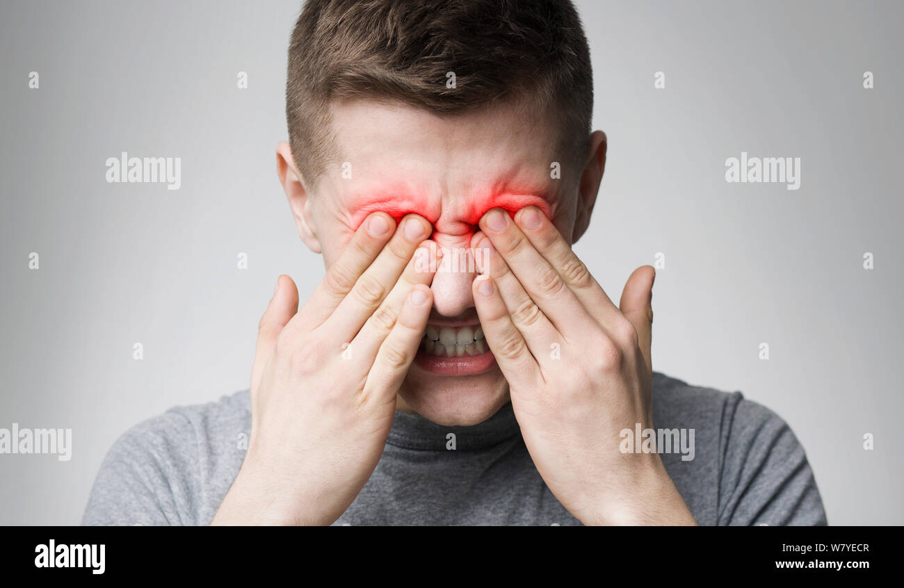 Tired man suffering from eye pain, rubbing red sore zone Stock Photo